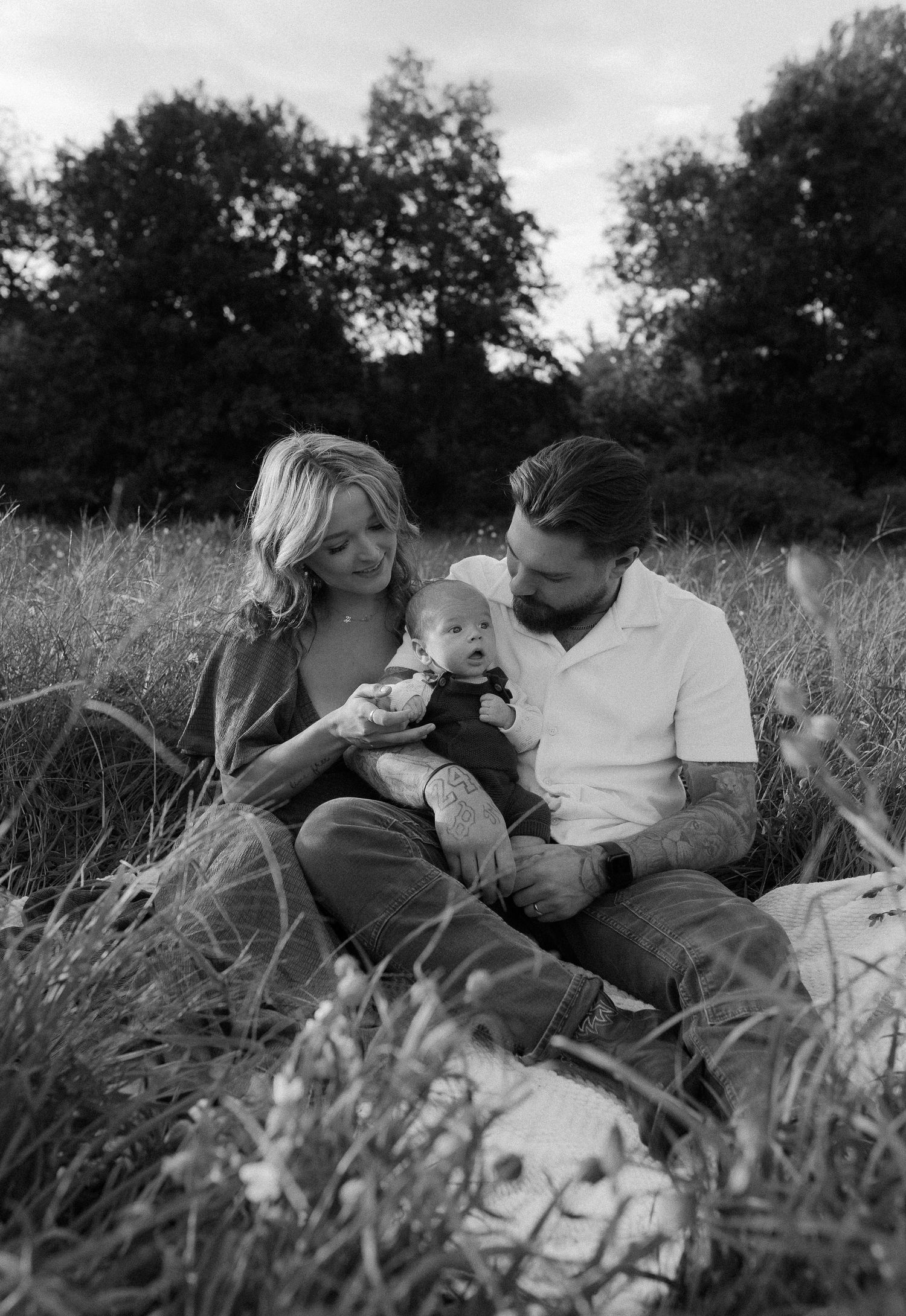 Black and white photo of a family cuddling together in a meadow of tall grass.
