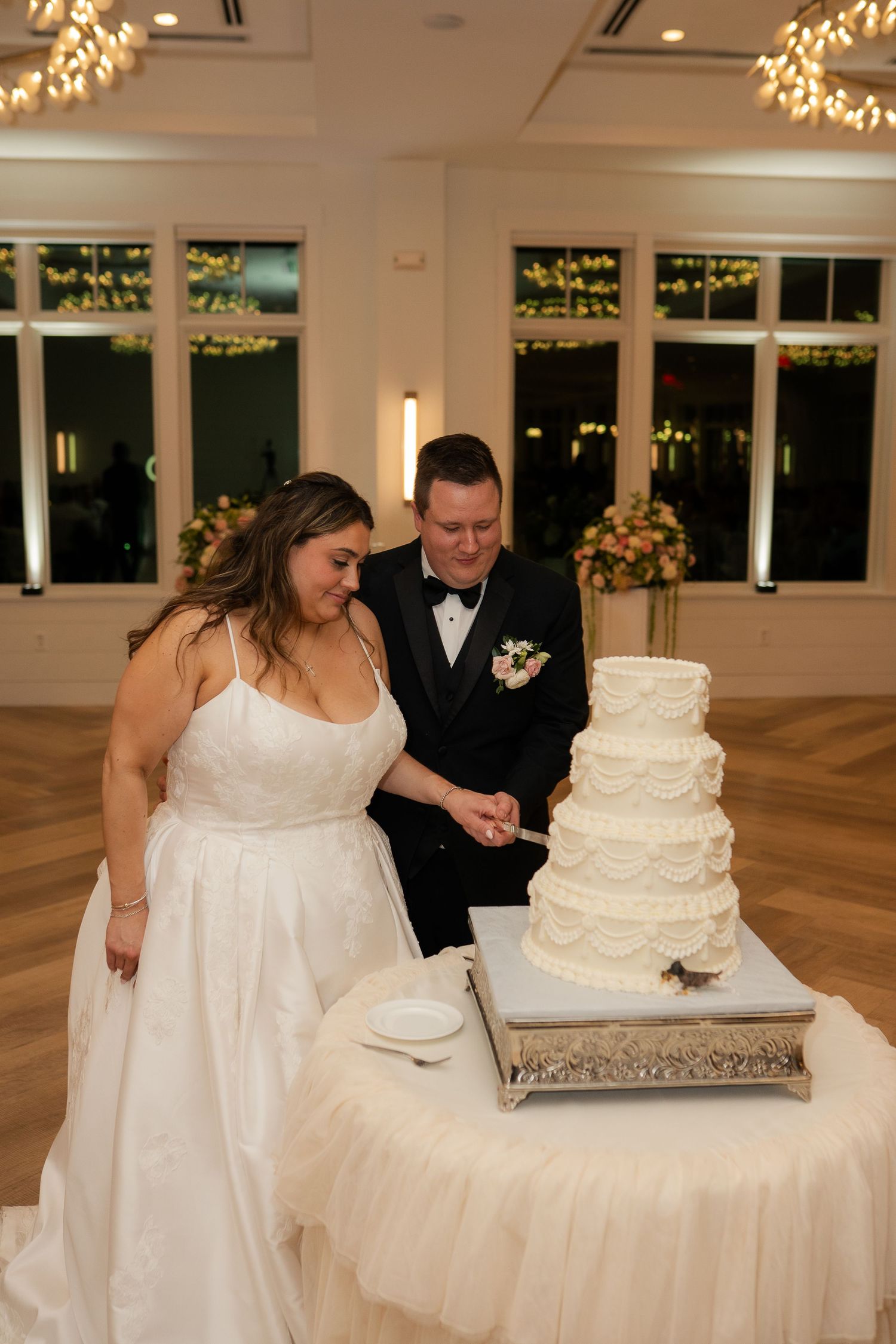Bride and groom cut four-tier white wedding cake together at elegant evening reception.