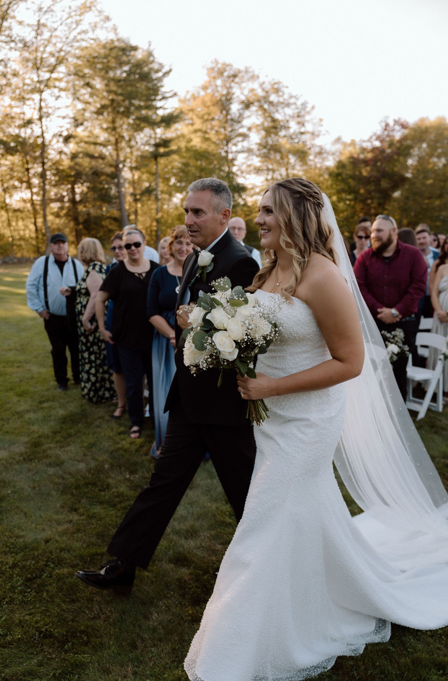 Wedding celebration with guests and couple on grassy lawn during golden hour.