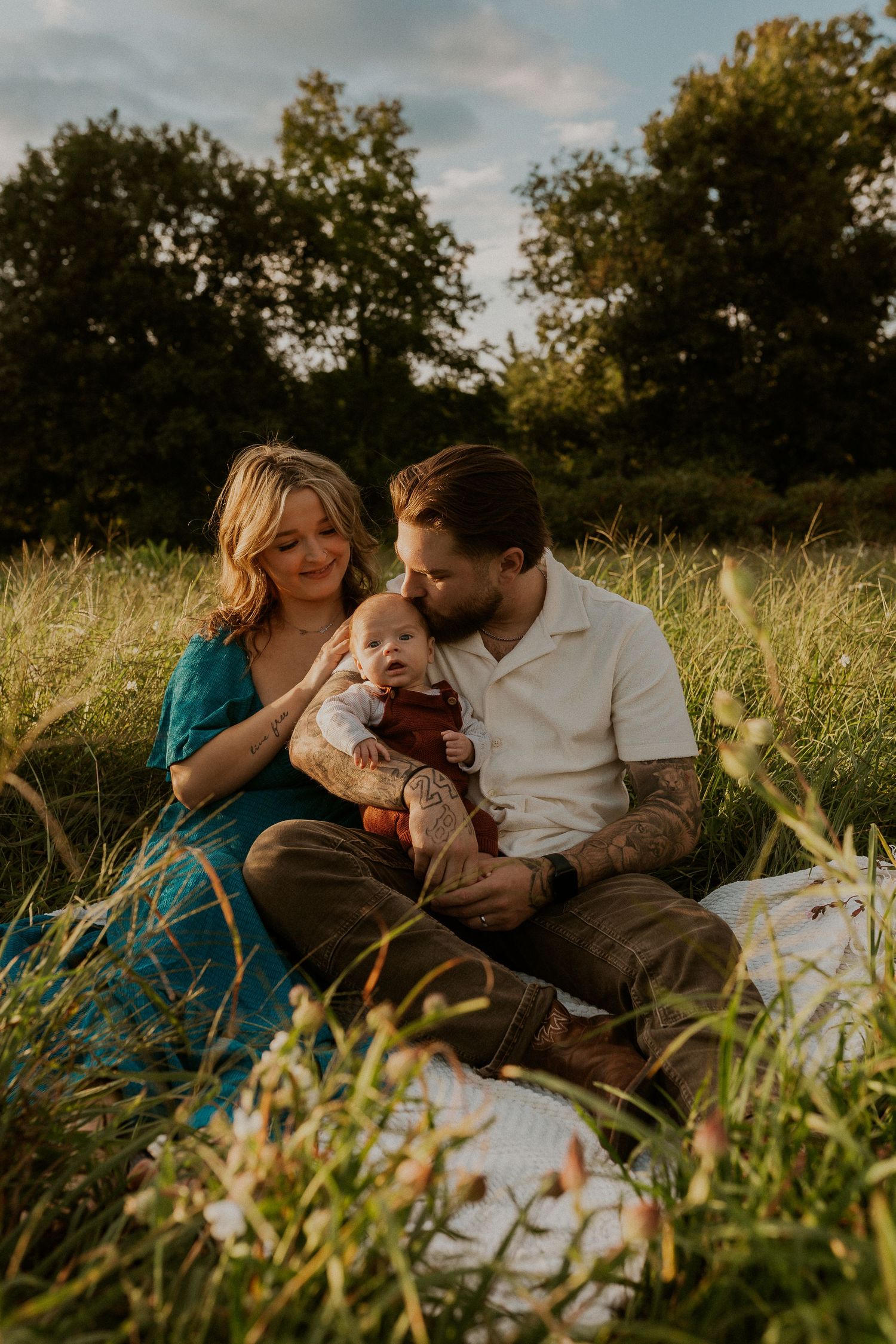 Family sitting together on blanket in golden meadow during sunset.