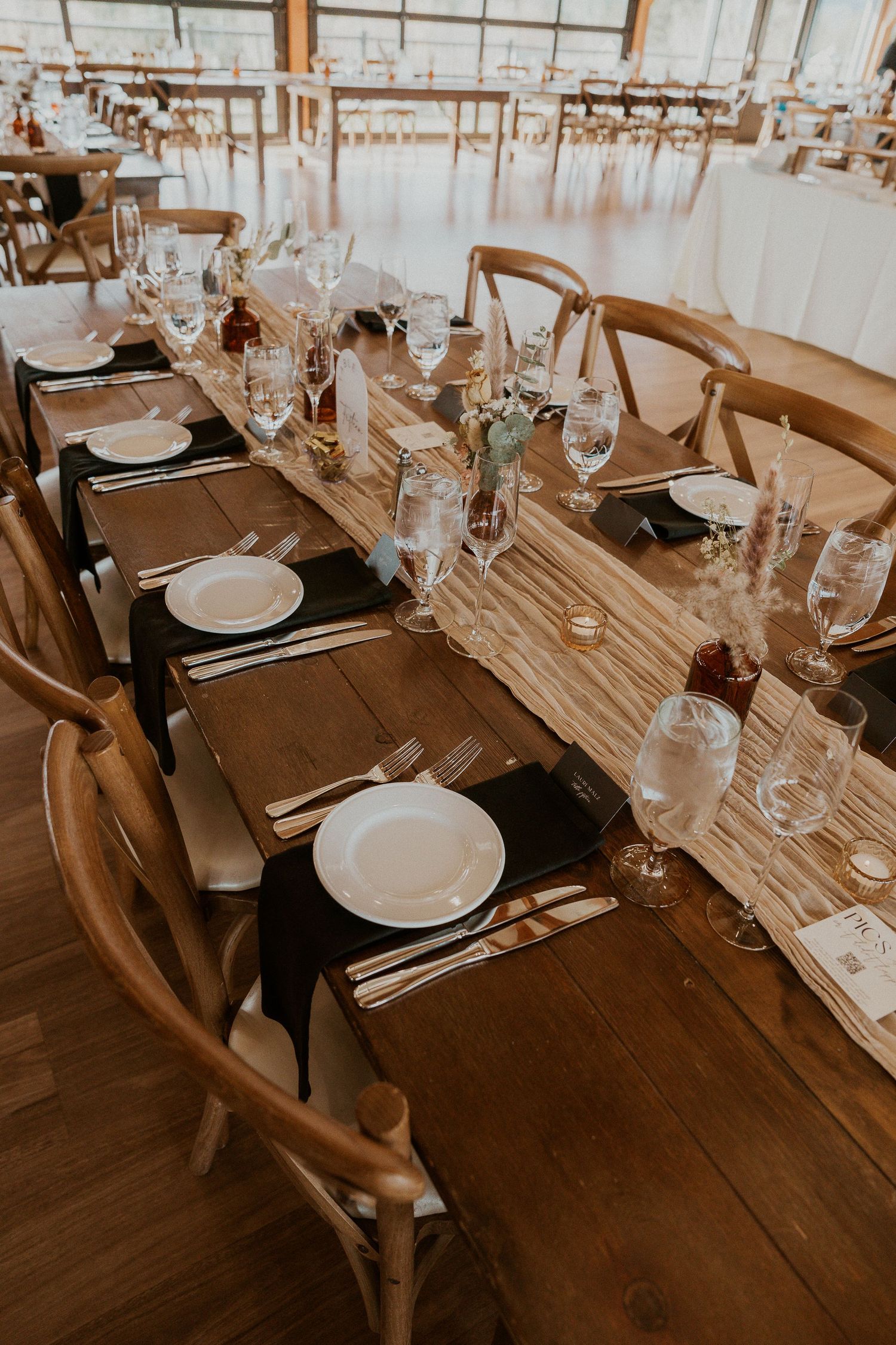 Rustic wooden farm tables set for an elegant wedding reception with white plates and wine glasses.
