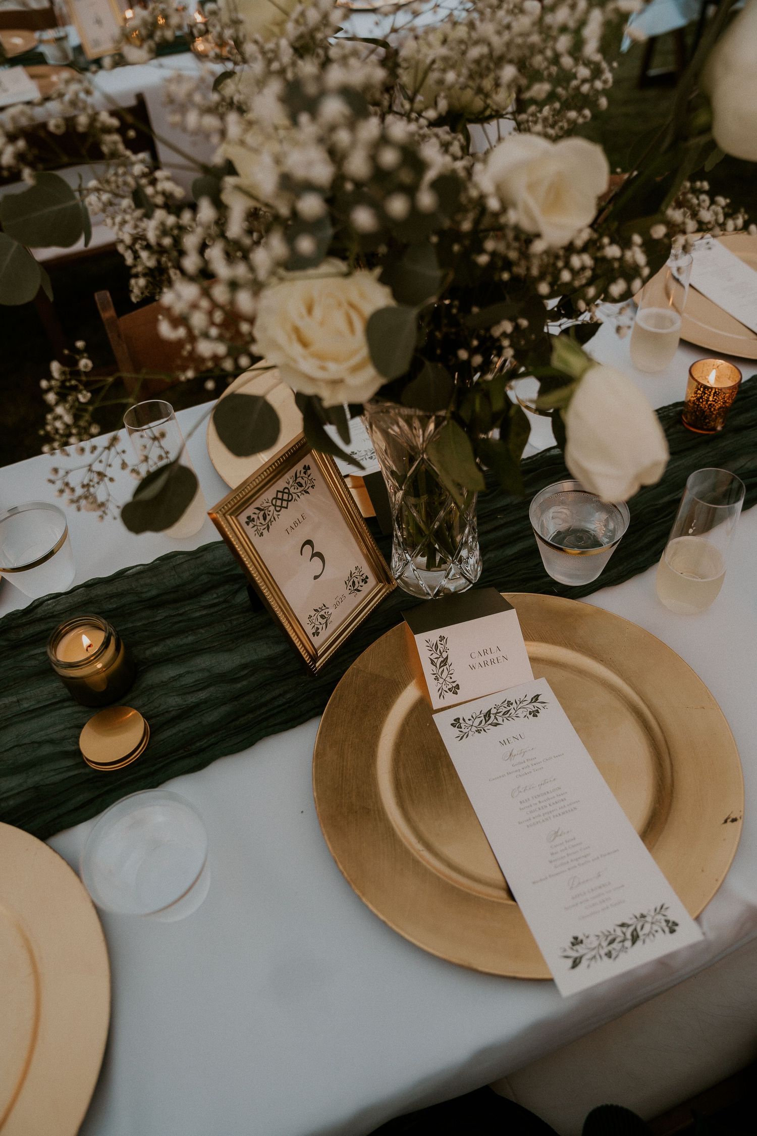 Elegant wedding table setting with gold charger plates, white roses, and decorative menu cards.