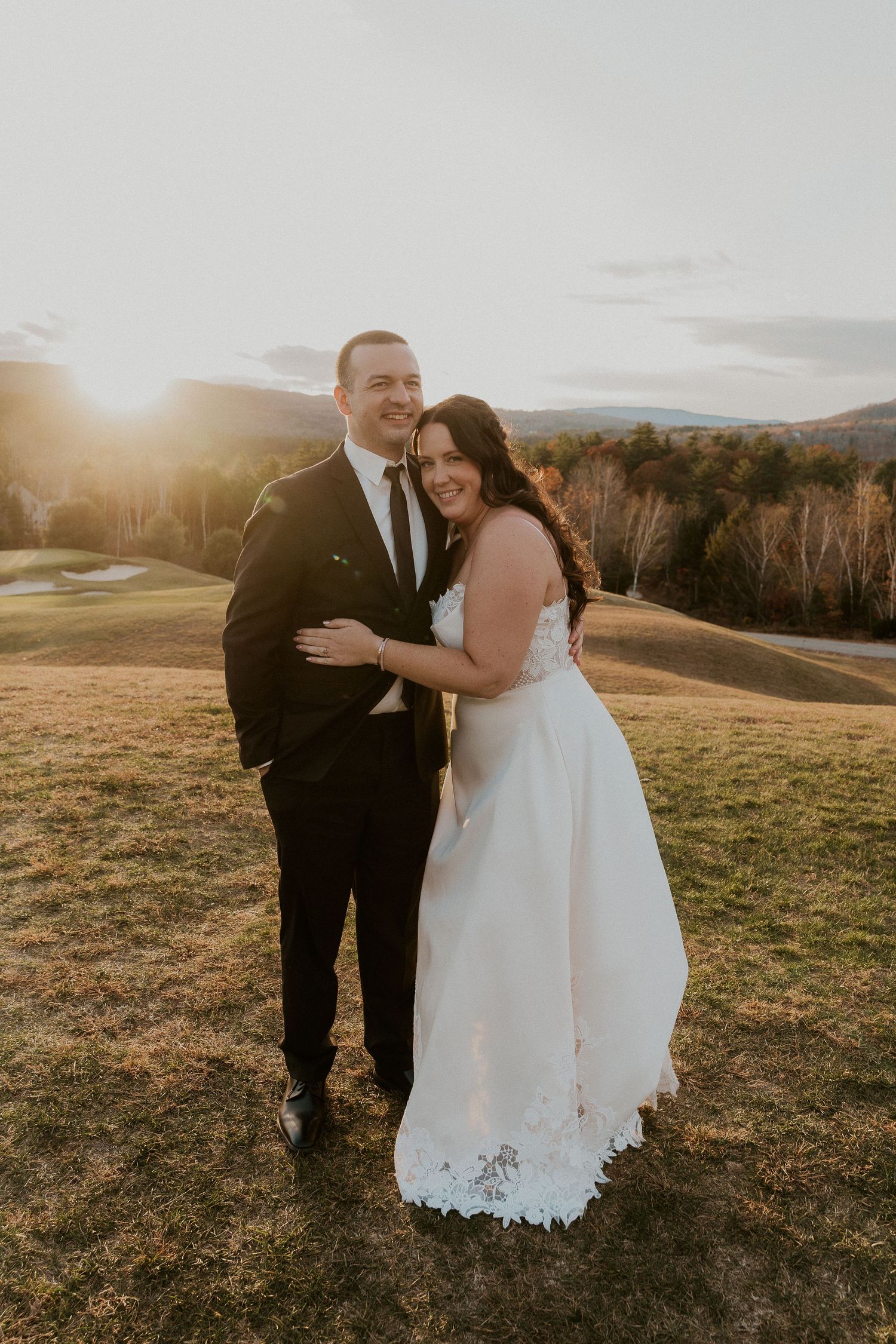 Couple sharing an intimate moment at sunset in an outdoor wedding setting with rolling hills in background.