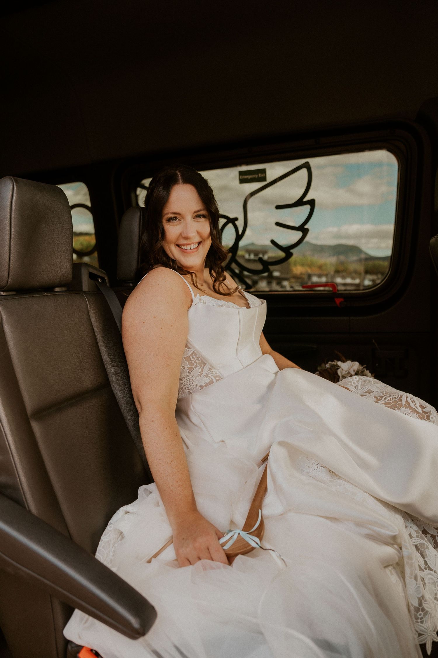 A wedding dress with lace details photographed in the backseat of a car with mountains visible through window.
