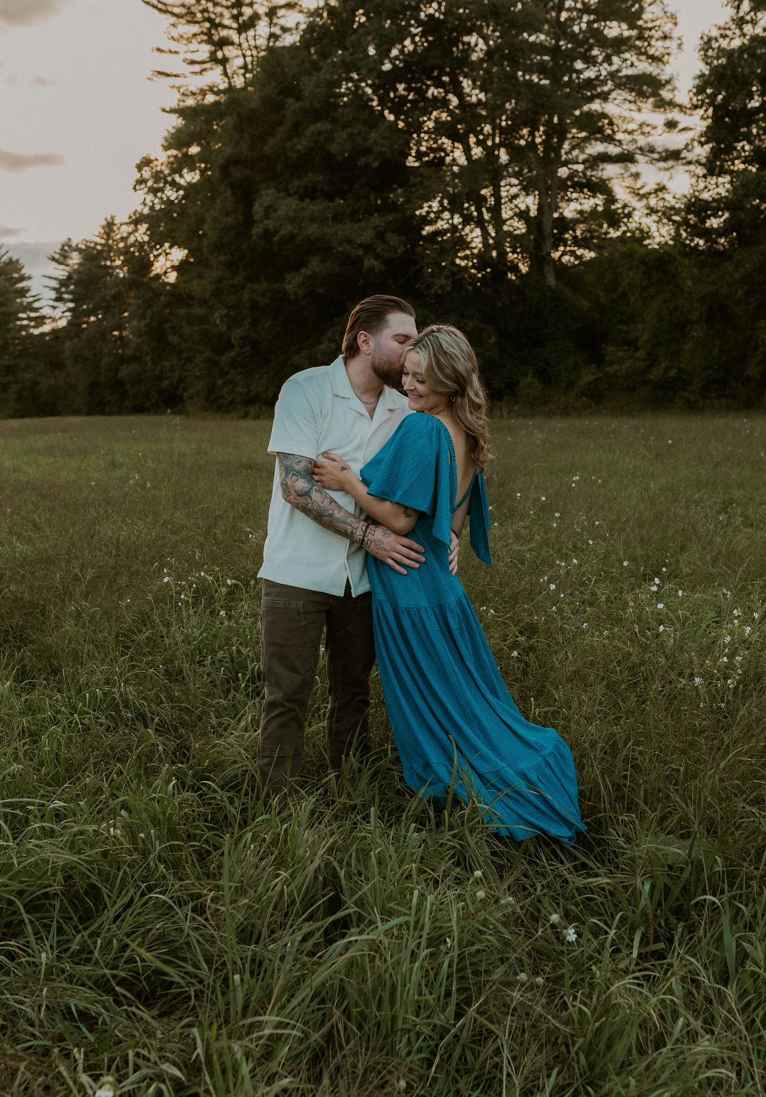 Romantic couple embracing in tall grass field during sunset.