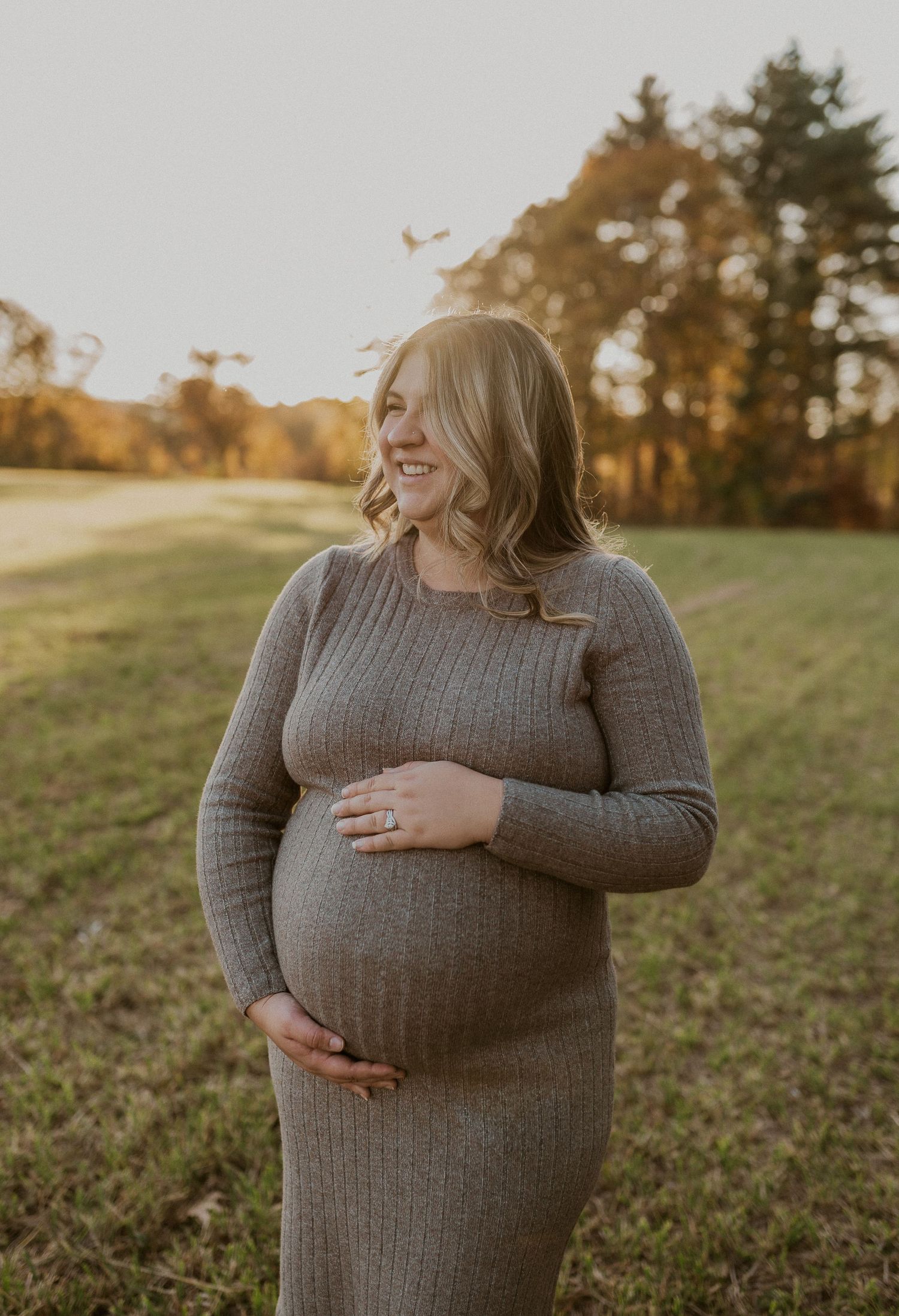 Pregnant woman in gray sweater holding belly during golden hour photoshoot.
