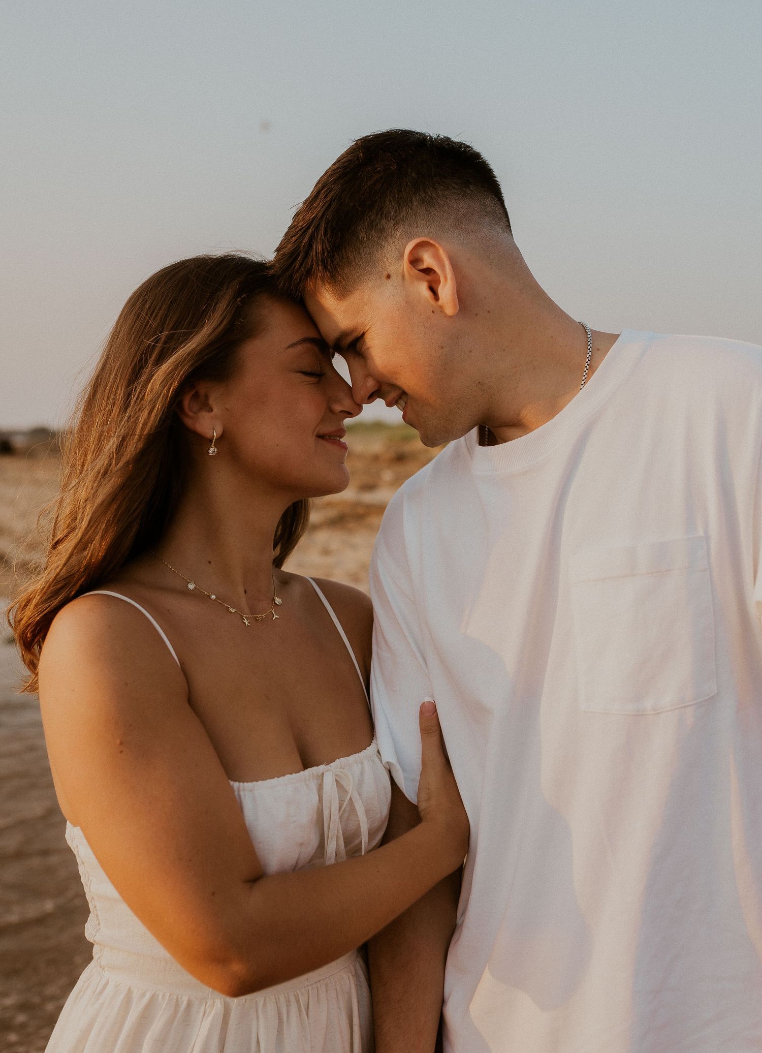 Close-up shots of a couple in white clothing sharing intimate moments on a beach at dusk.