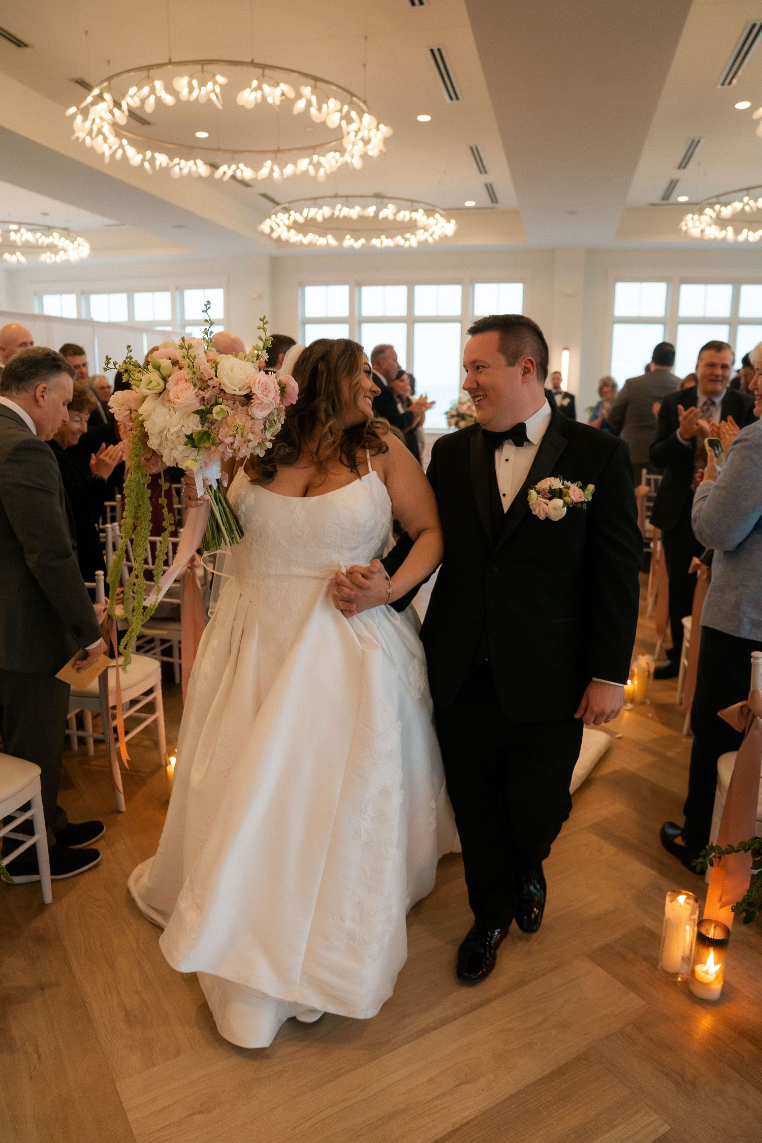 Newlyweds walking back down aisle smiling at each other after wedding ceremony with candles lit.