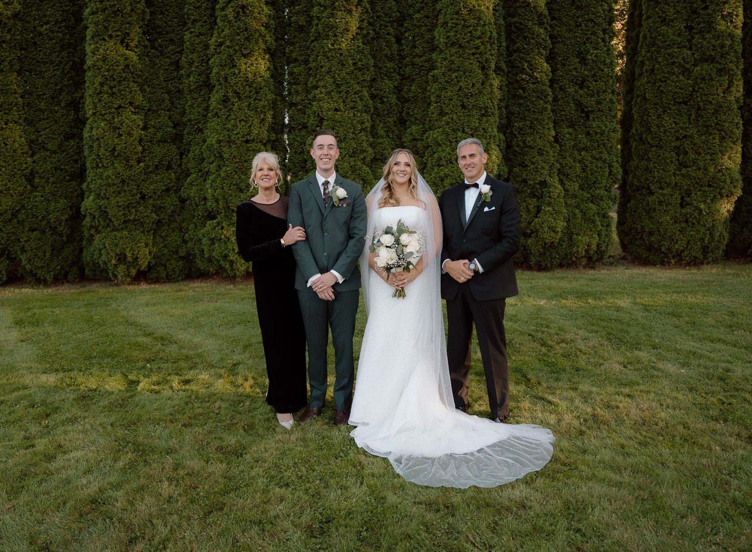 Small wedding party group photo in front of tall green cypress trees.