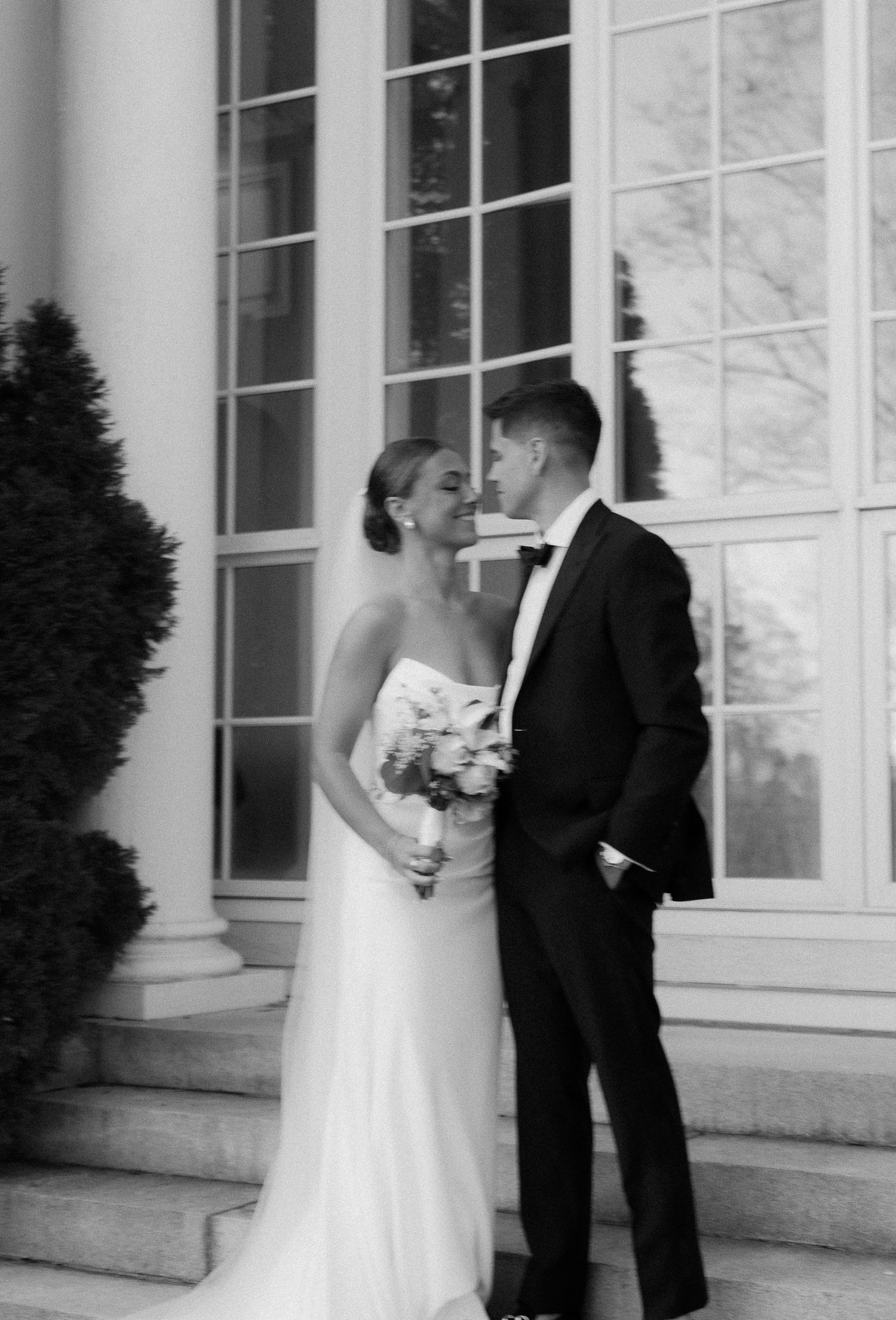 Black and white photo of smiling bride and groom sharing a tender moment on venue steps.