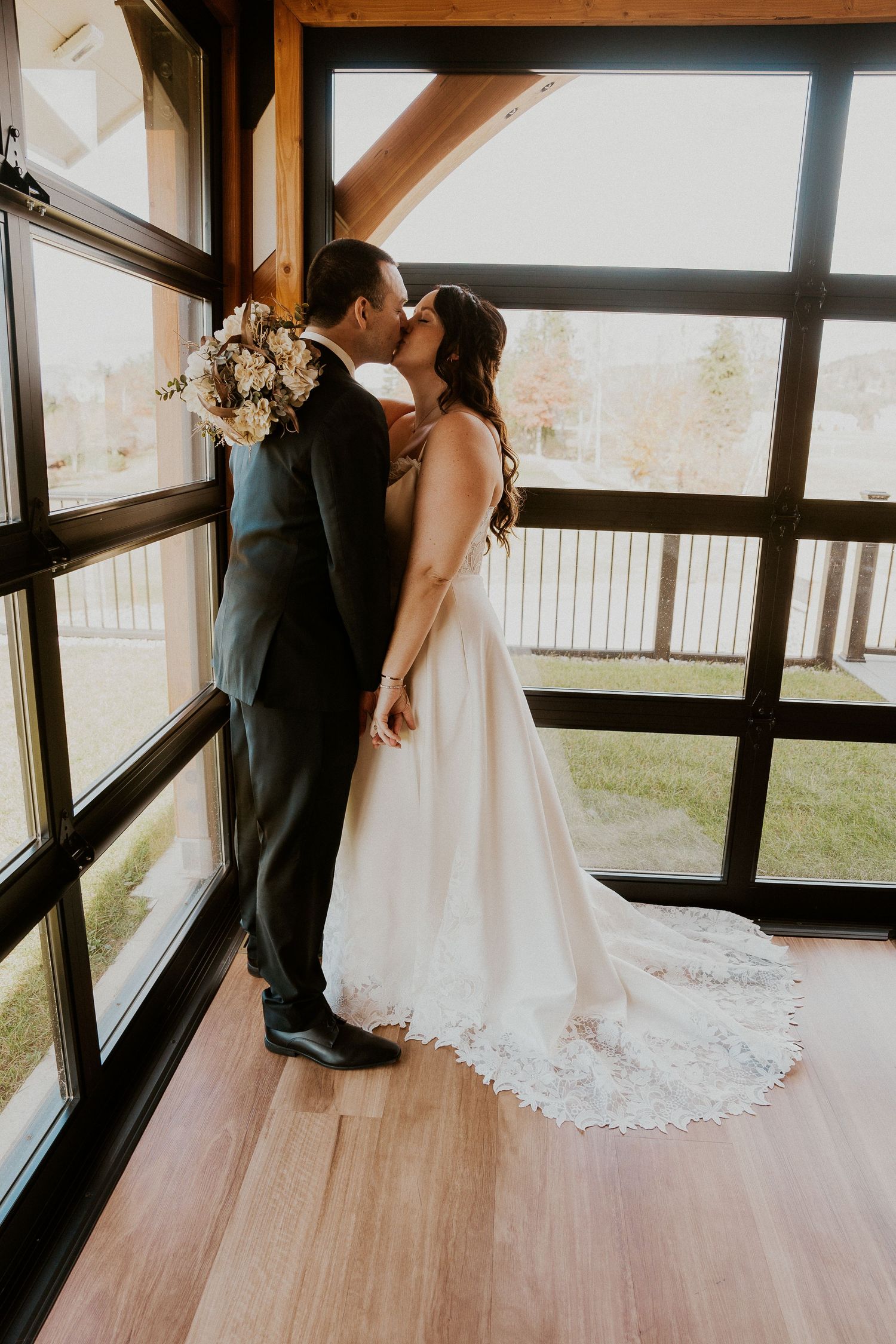 Wedding couple dancing together in an indoor venue with large windows and wooden beams.