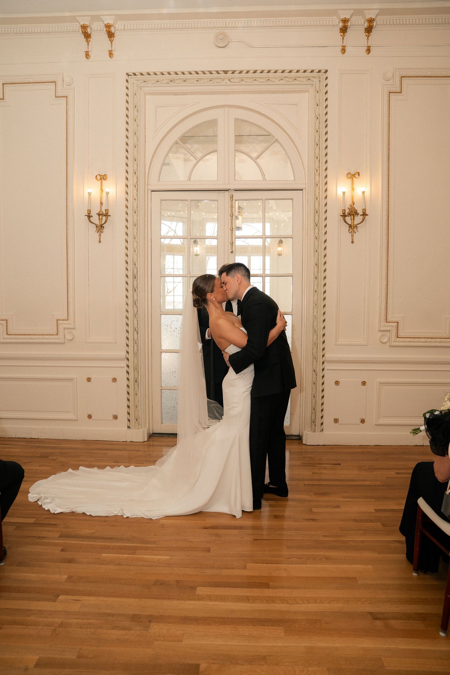 Newlyweds share their first kiss as husband and wife in a beautiful white ornate ballroom.
