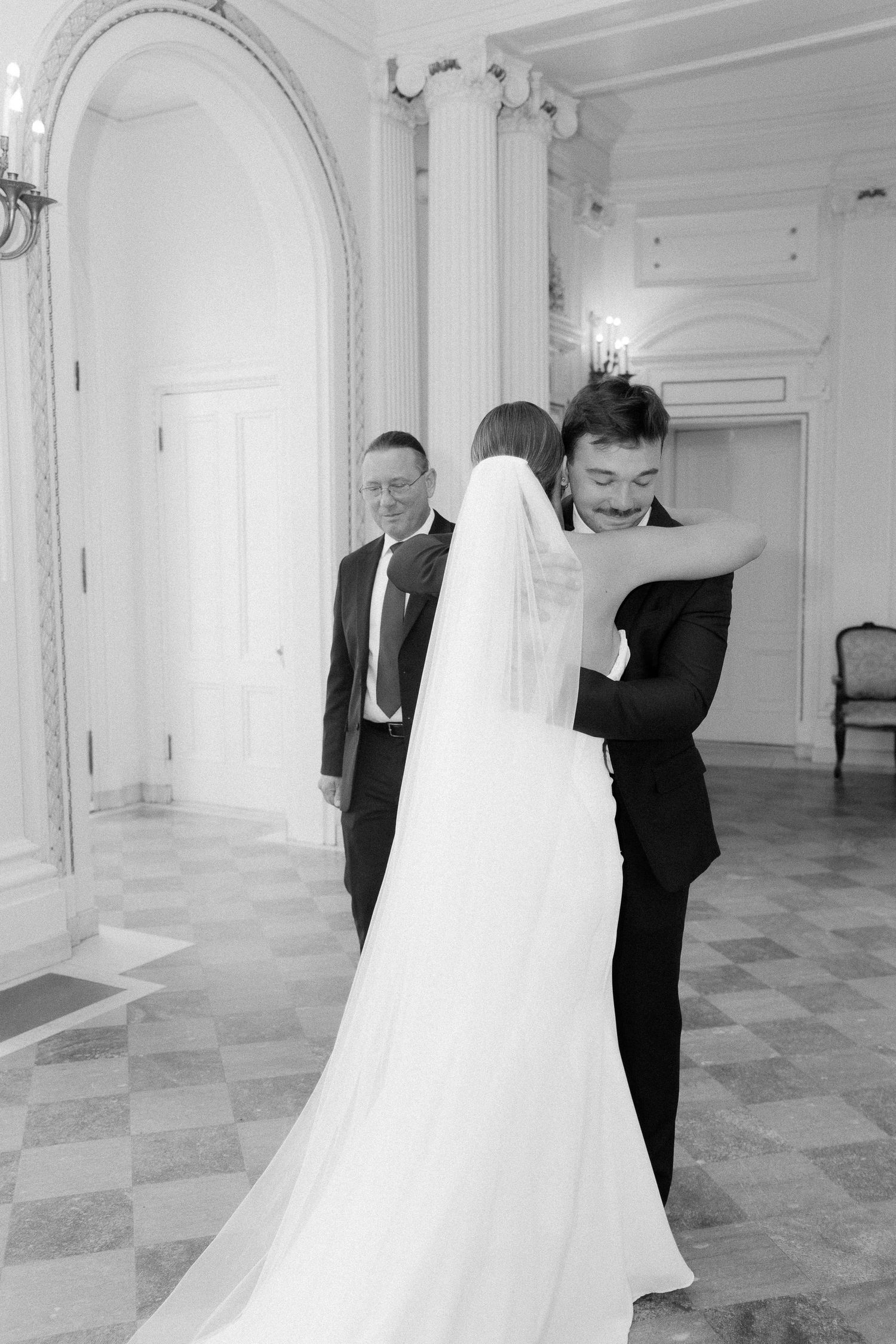 Black and white photo of a bride and groom embracing during their first look in an elegant ballroom.
