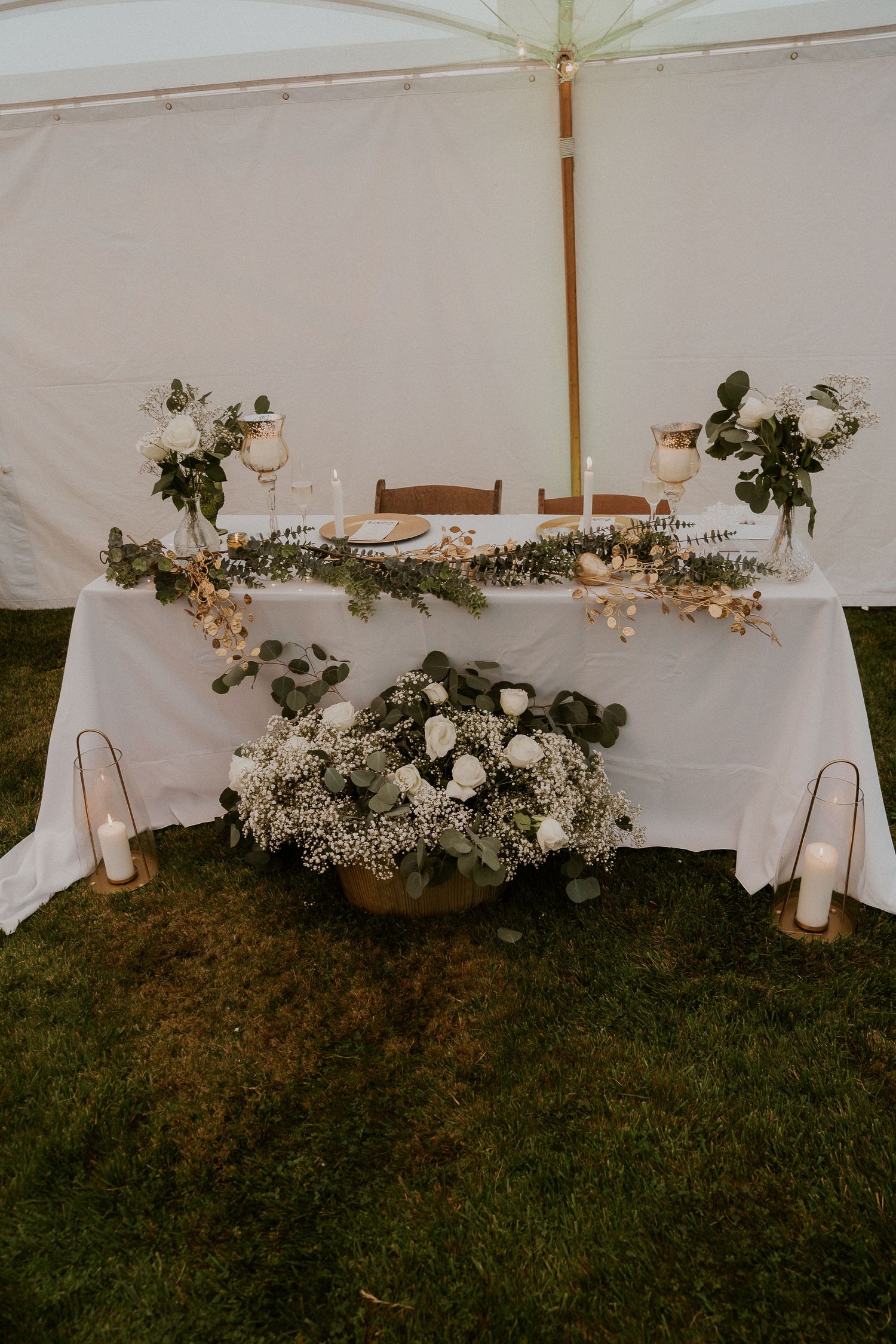 Elegant wedding reception table setup under white tent with floral decorations and candlelight.