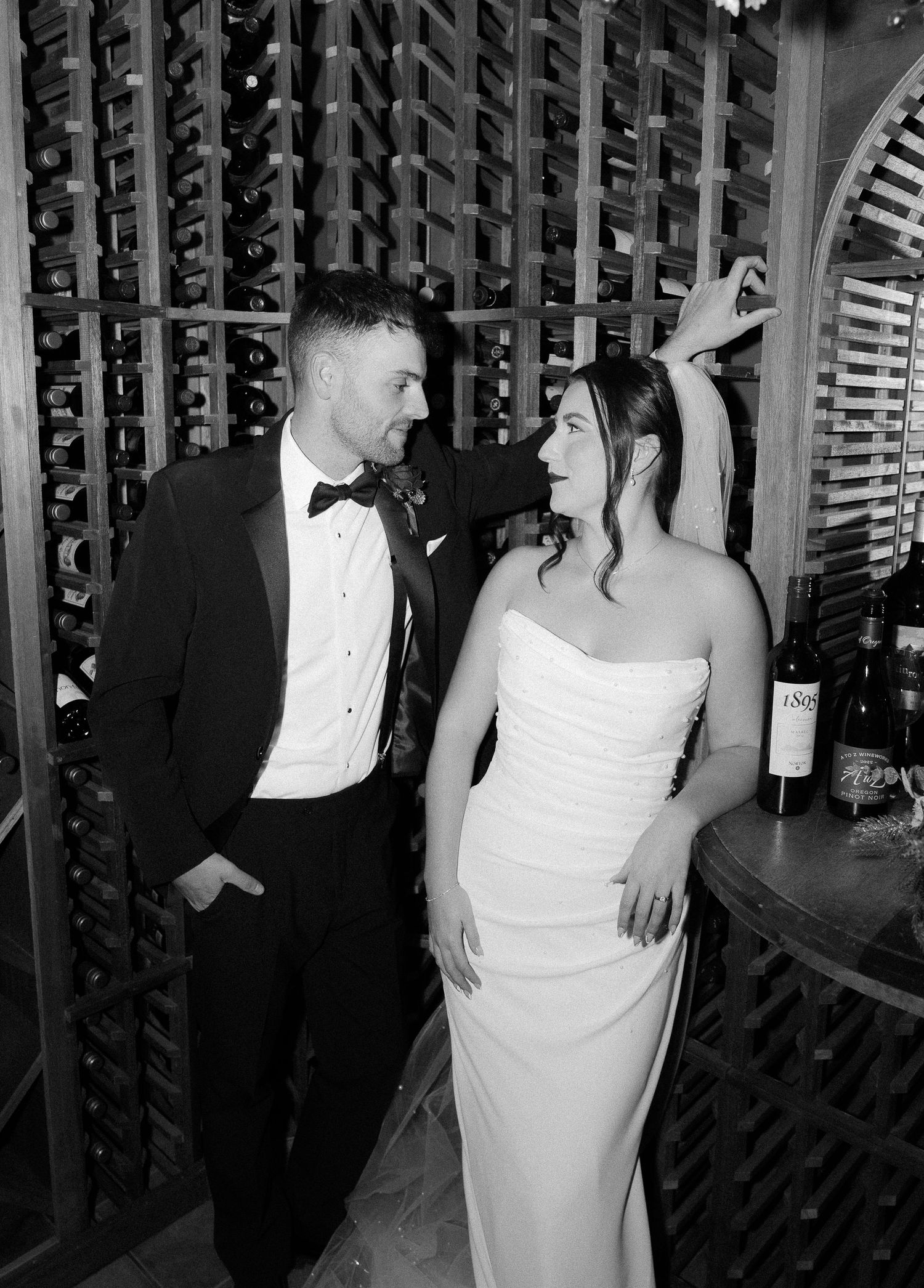 Black and white photo of a bride and groom posing in a wine cellar on their wedding day.