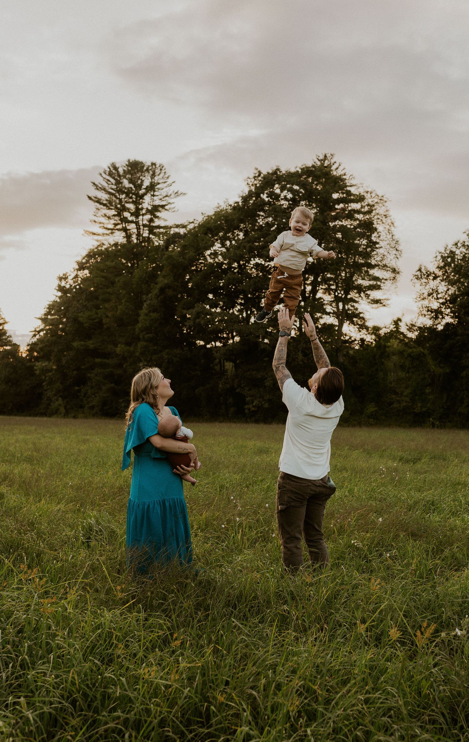 Playful family moment in grassy field with child being lifted high in the air.