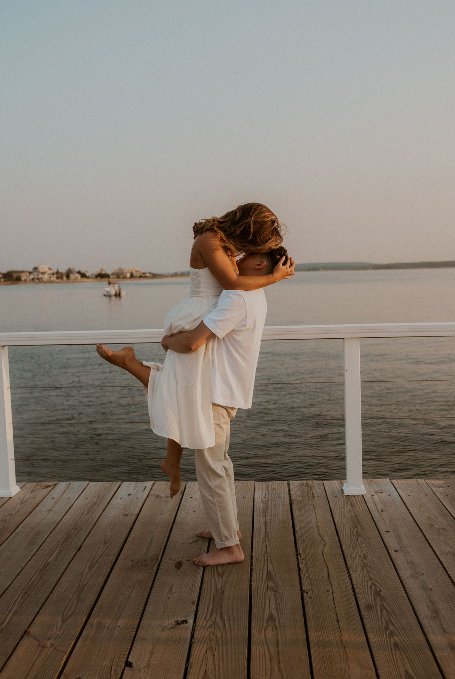 A couple embracing in a romantic lift pose on a wooden dock by the water.