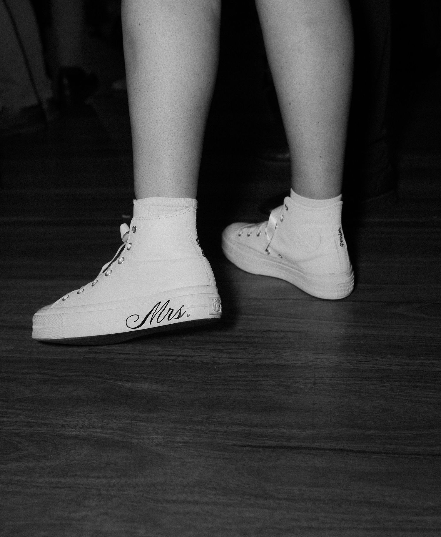Black and white photo showing white high-top sneakers with 'Nike' branding on a dark hardwood floor.