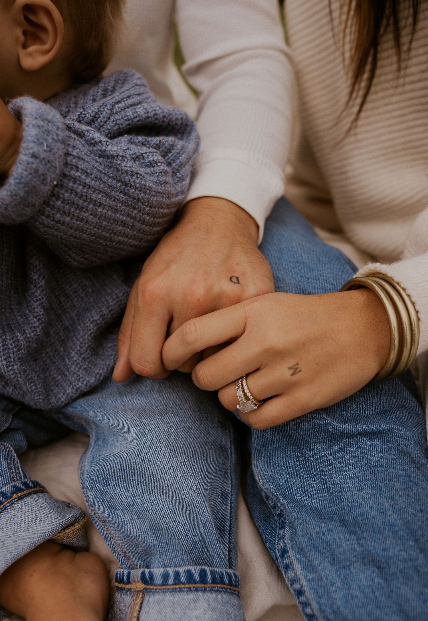 Close-up series of hands with rings and bracelets resting on denim jeans.