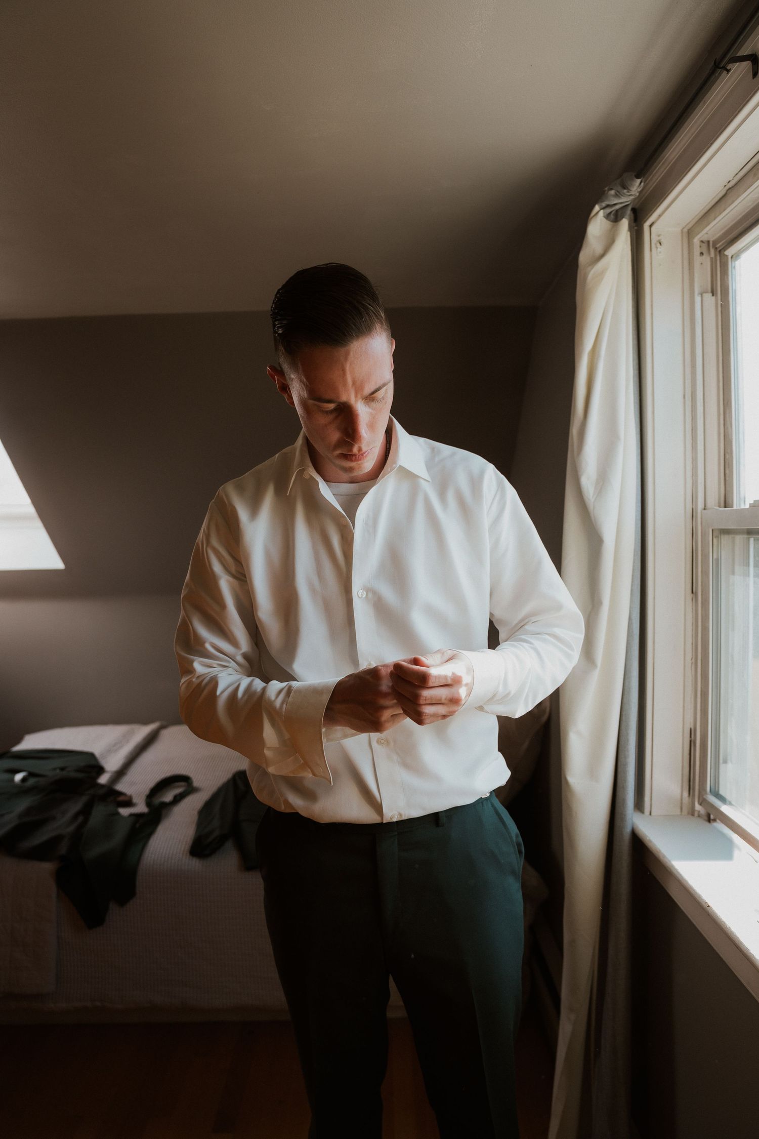 Someone in formal attire preparing by a window in moody lighting.