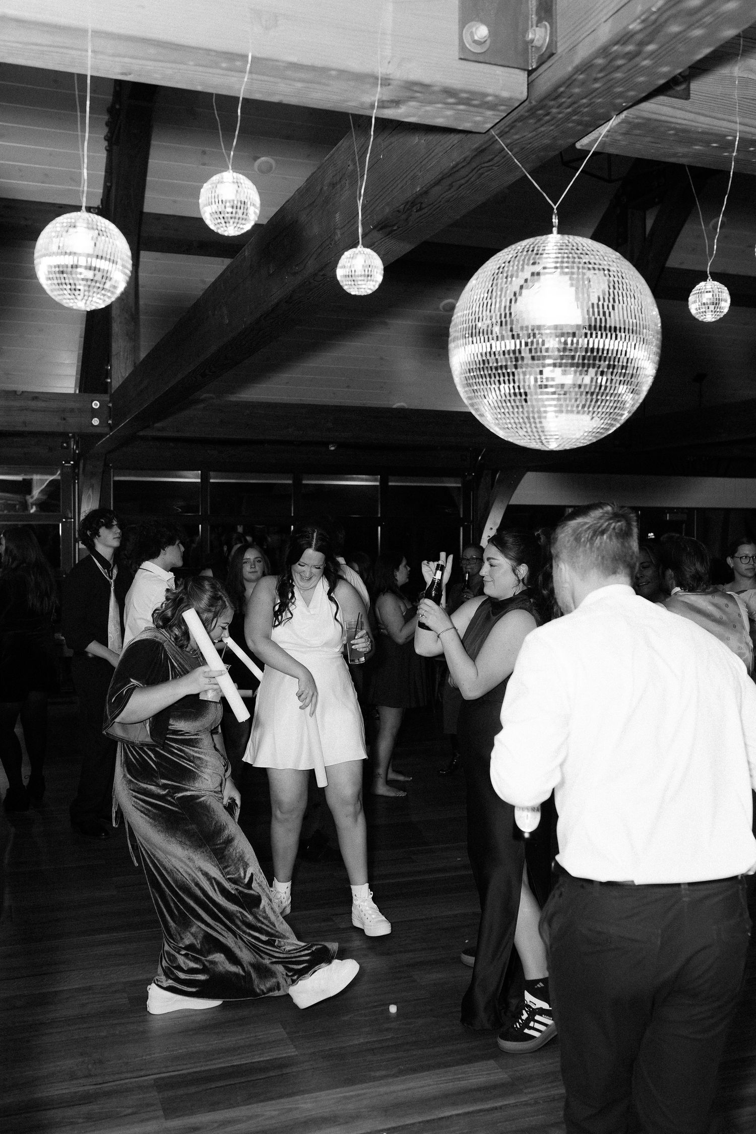 Dancers move under illuminated disco balls in a dark dance studio with wooden floors during a party or event.