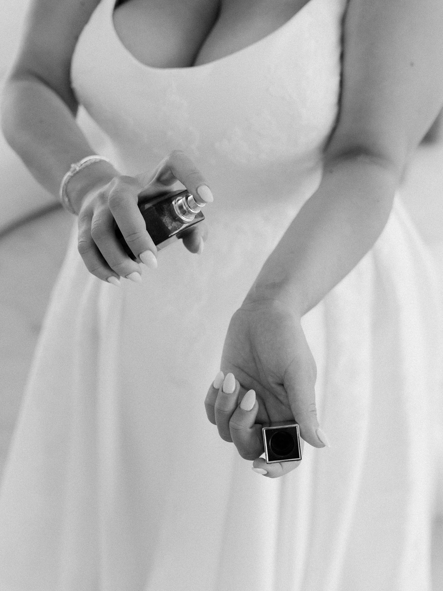 Bride in white wedding dress spraying perfume, elegant black and white bridal preparation photo.