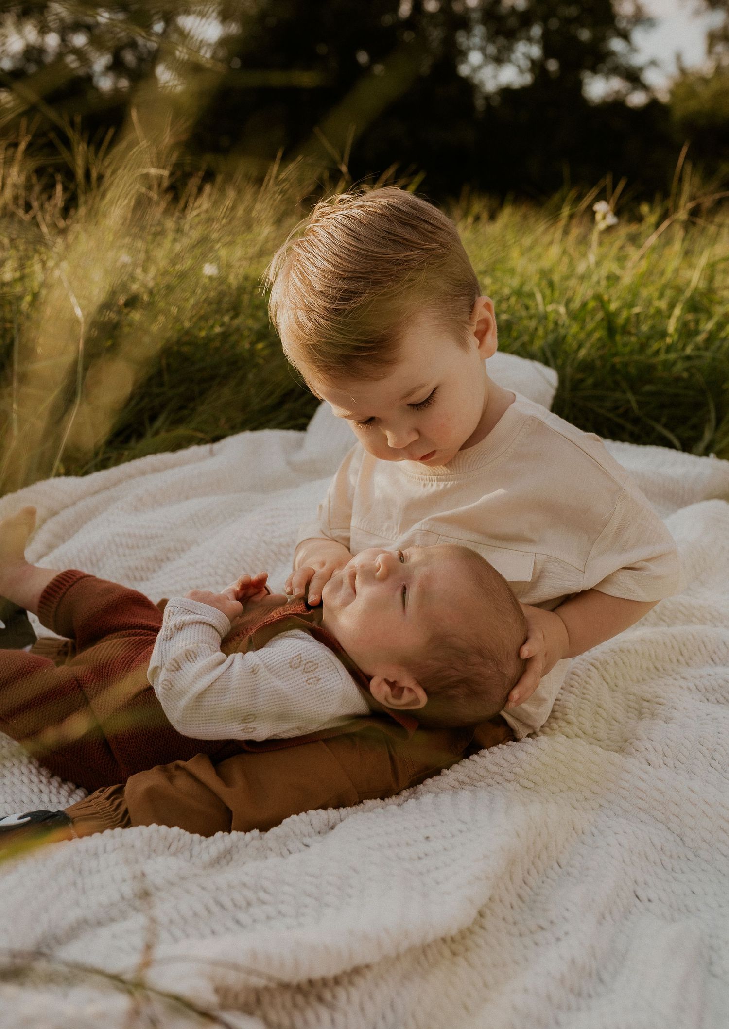 Two siblings sharing tender moment on white blanket in grass.