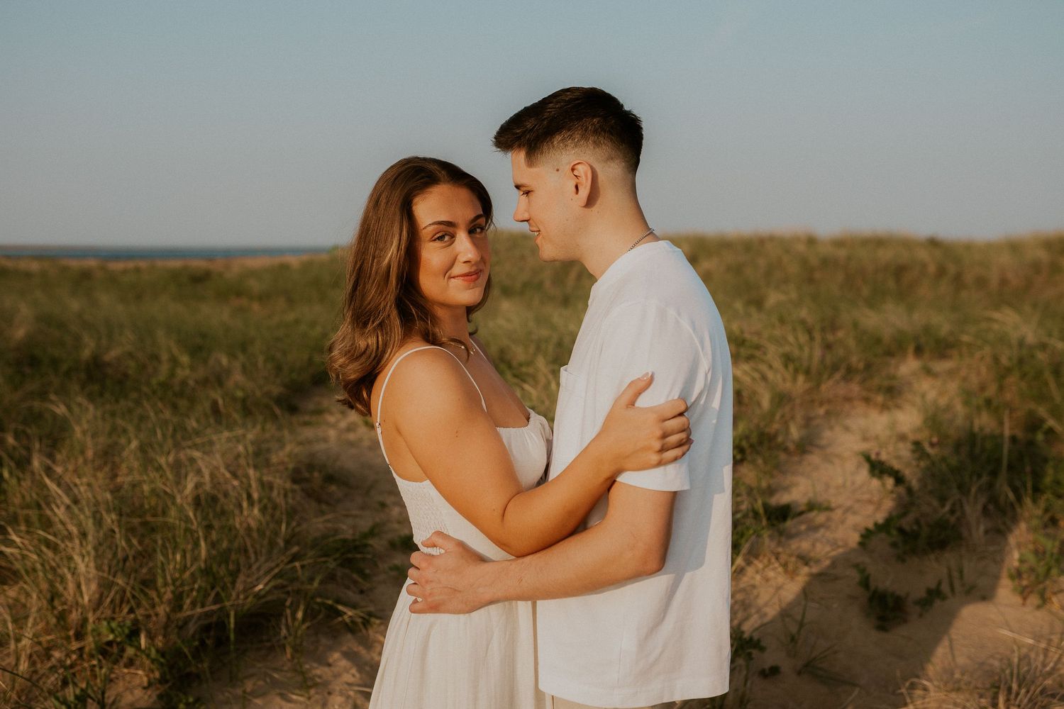 Warm-toned photos of a couple sharing romantic moments on a sandy trail during sunset.