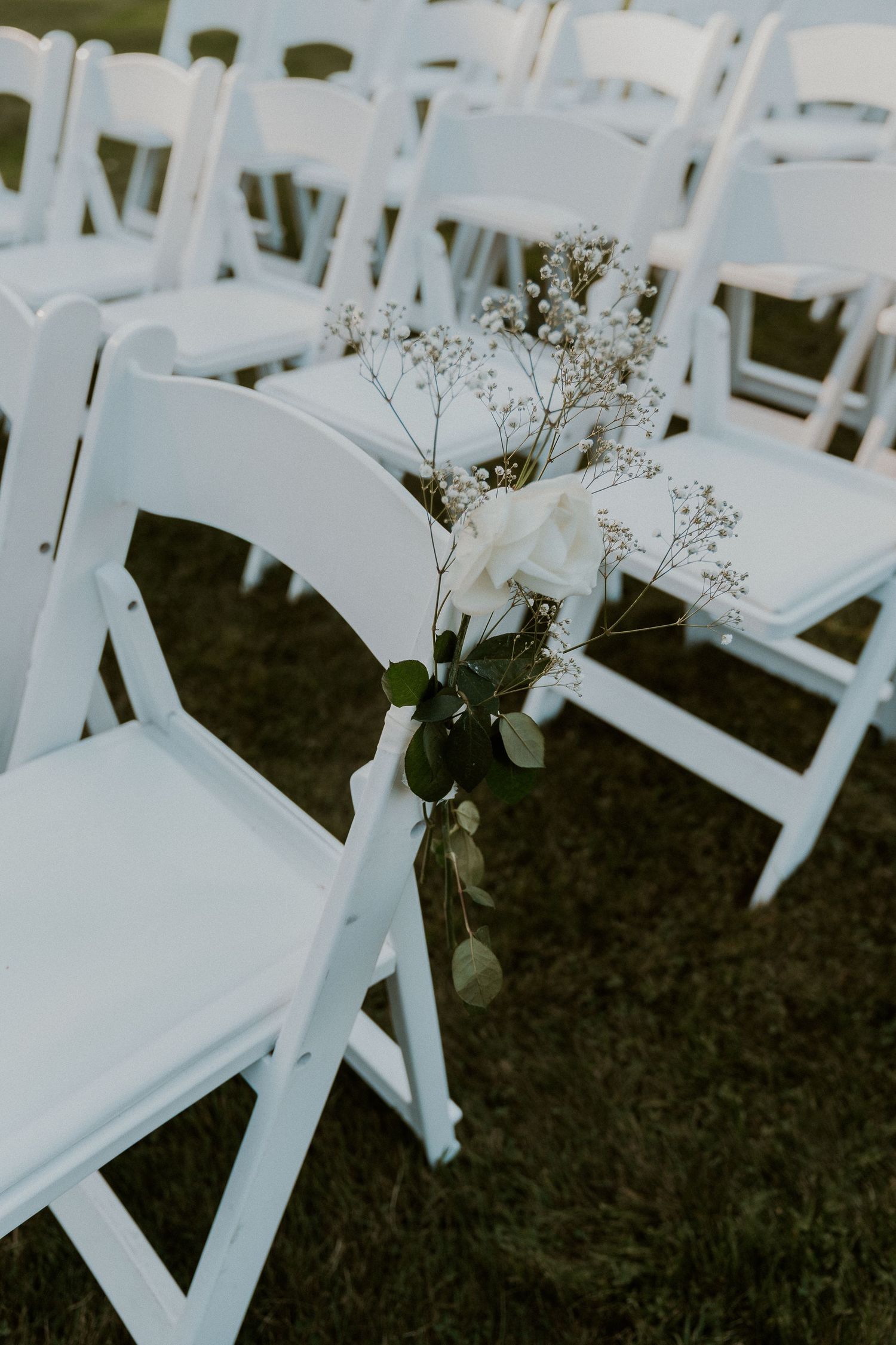 White folding chairs decorated with floral arrangements for an outdoor wedding ceremony.