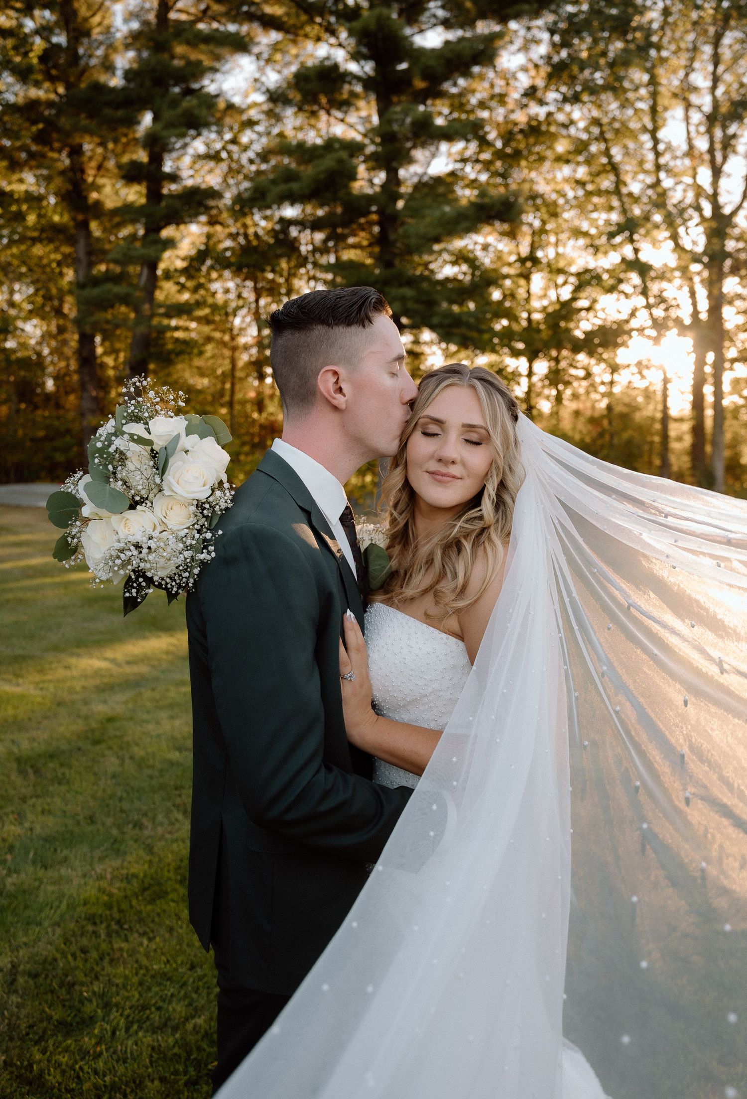 Romantic wedding photos at sunset showing a couple embracing with a flowing veil in a grassy outdoor setting.