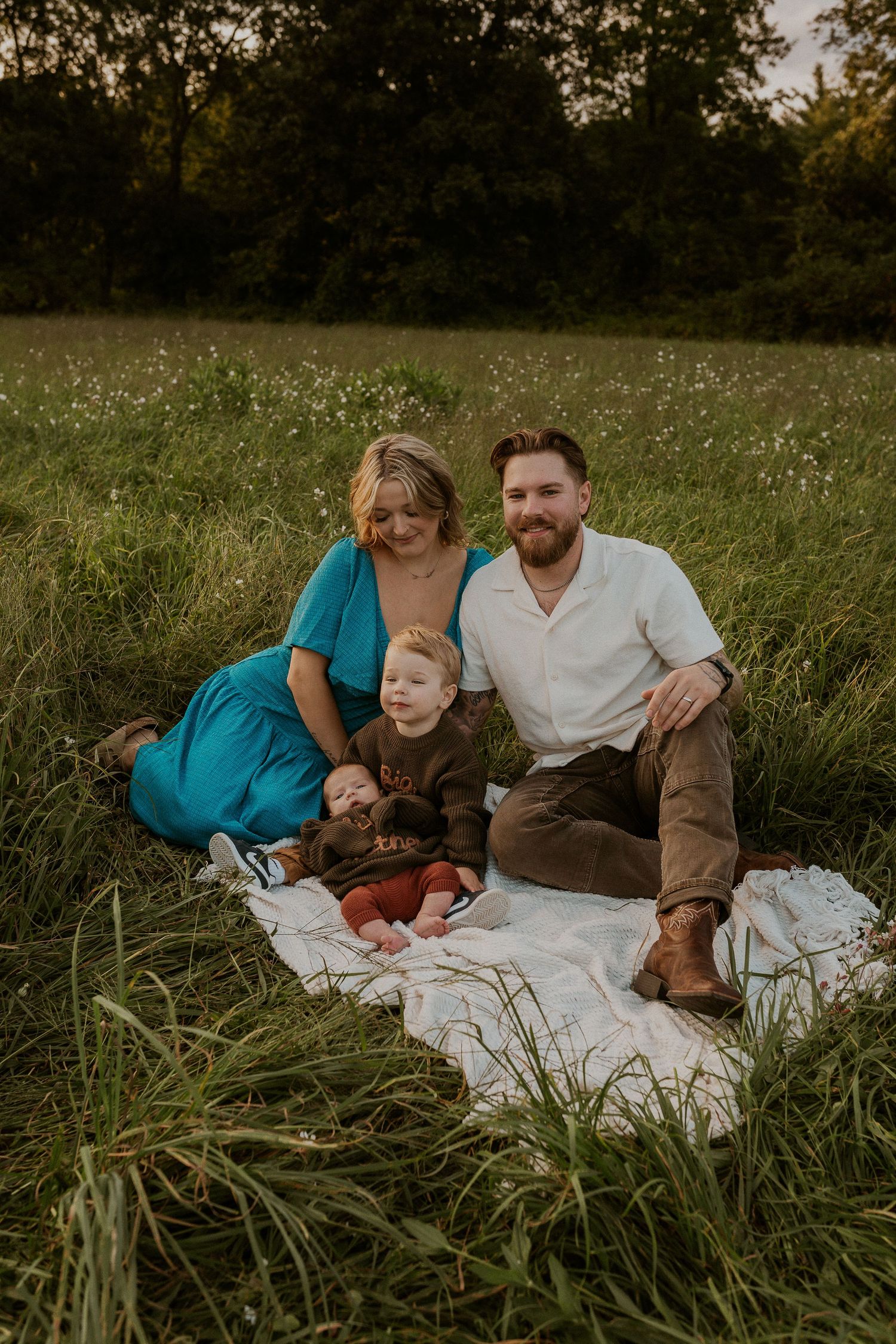 Family of four relaxing on white blanket in sunlit meadow during golden hour.