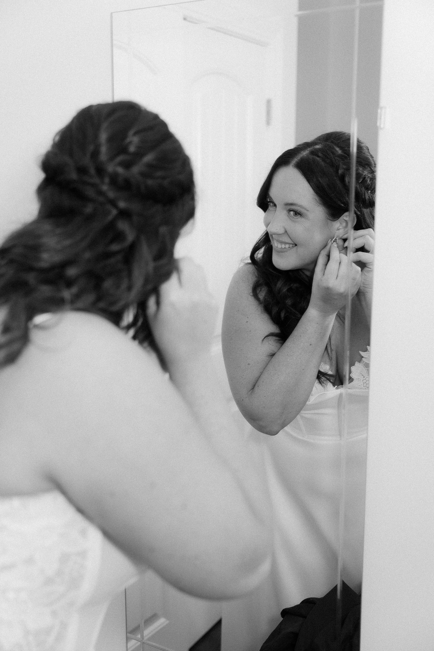 Black and white series showing preparation of bridal hair and makeup in bathroom mirror.