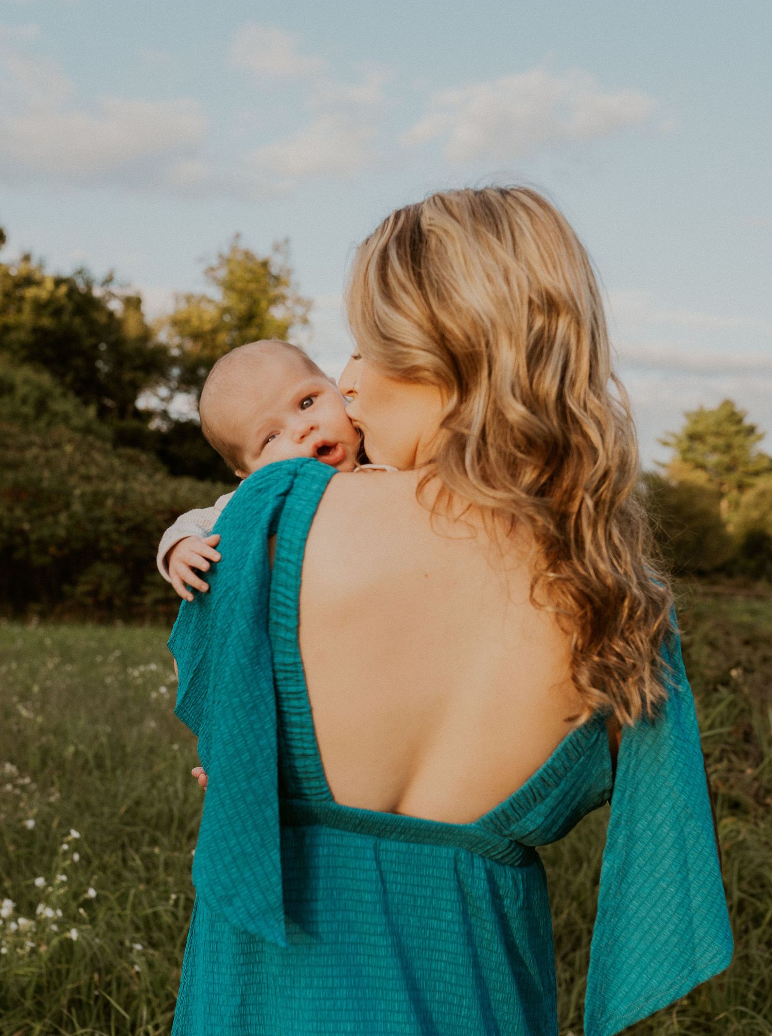 A tender embrace captured in a turquoise dress against a sunset meadow backdrop.