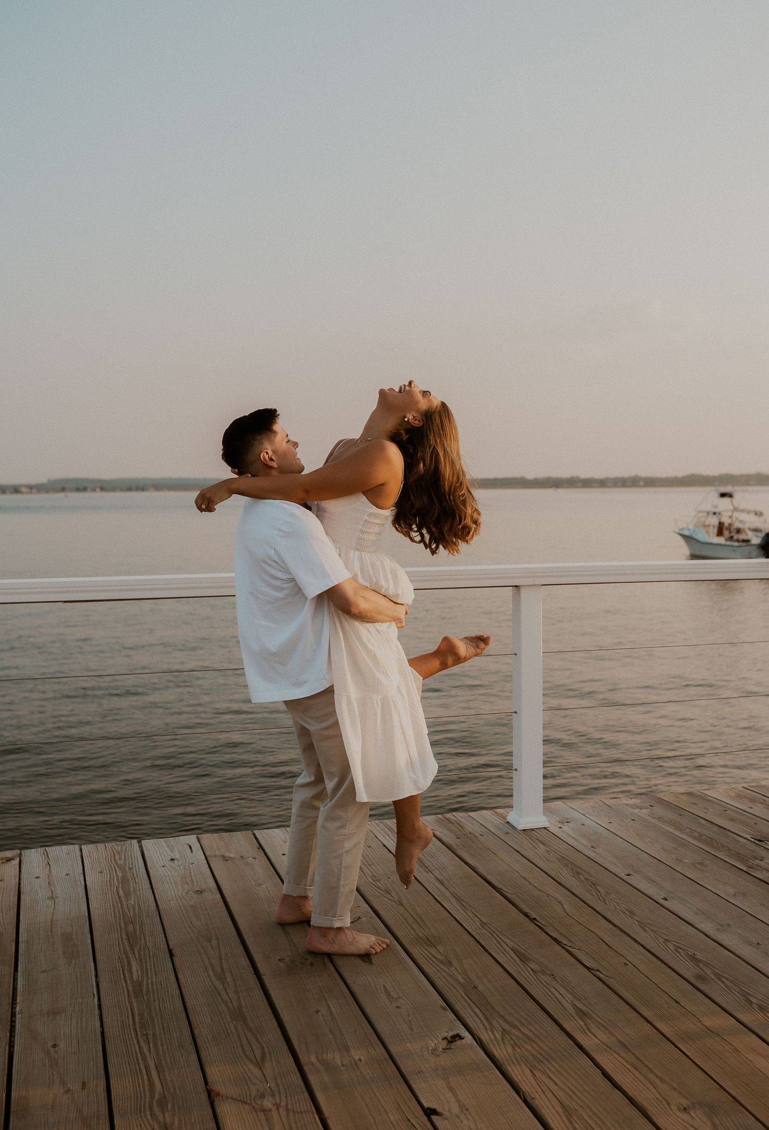 A playful couple dancing and embracing on a wooden pier at sunset.
