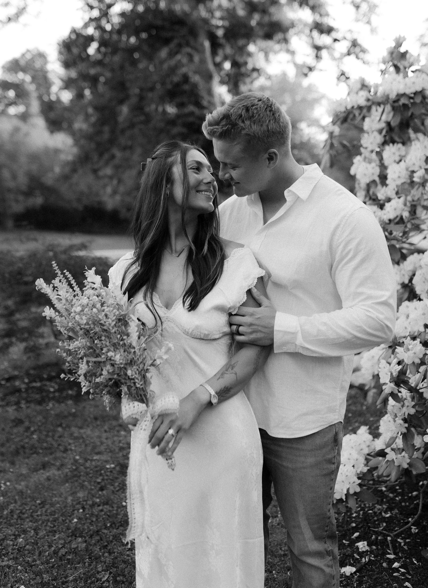 Couple in white outfits sharing intimate moments among spring blossoms.