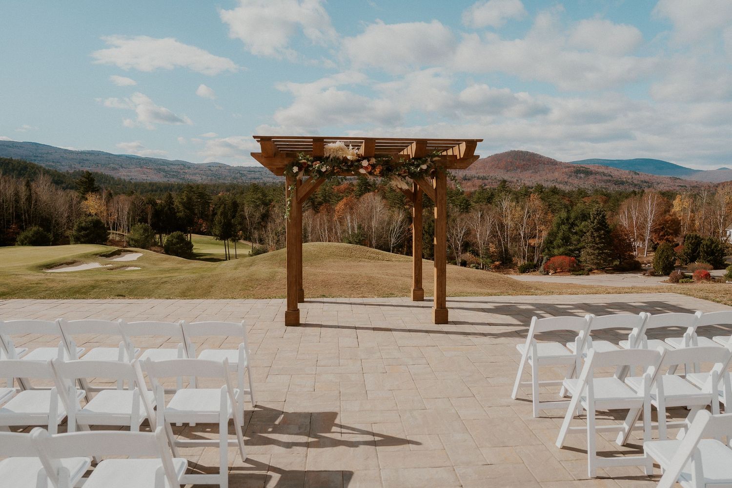 White chairs set up for an outdoor wedding ceremony with mountain views and wooden arch in a desert landscape.