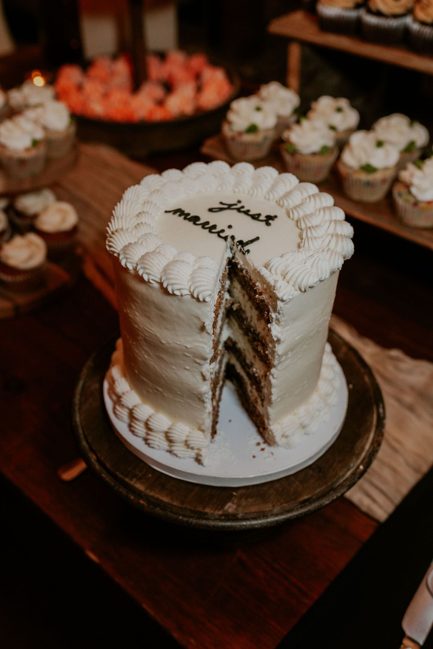 A white frosted layer cake with decorative piping is shown being cut to reveal dark layers inside on a silver platter.