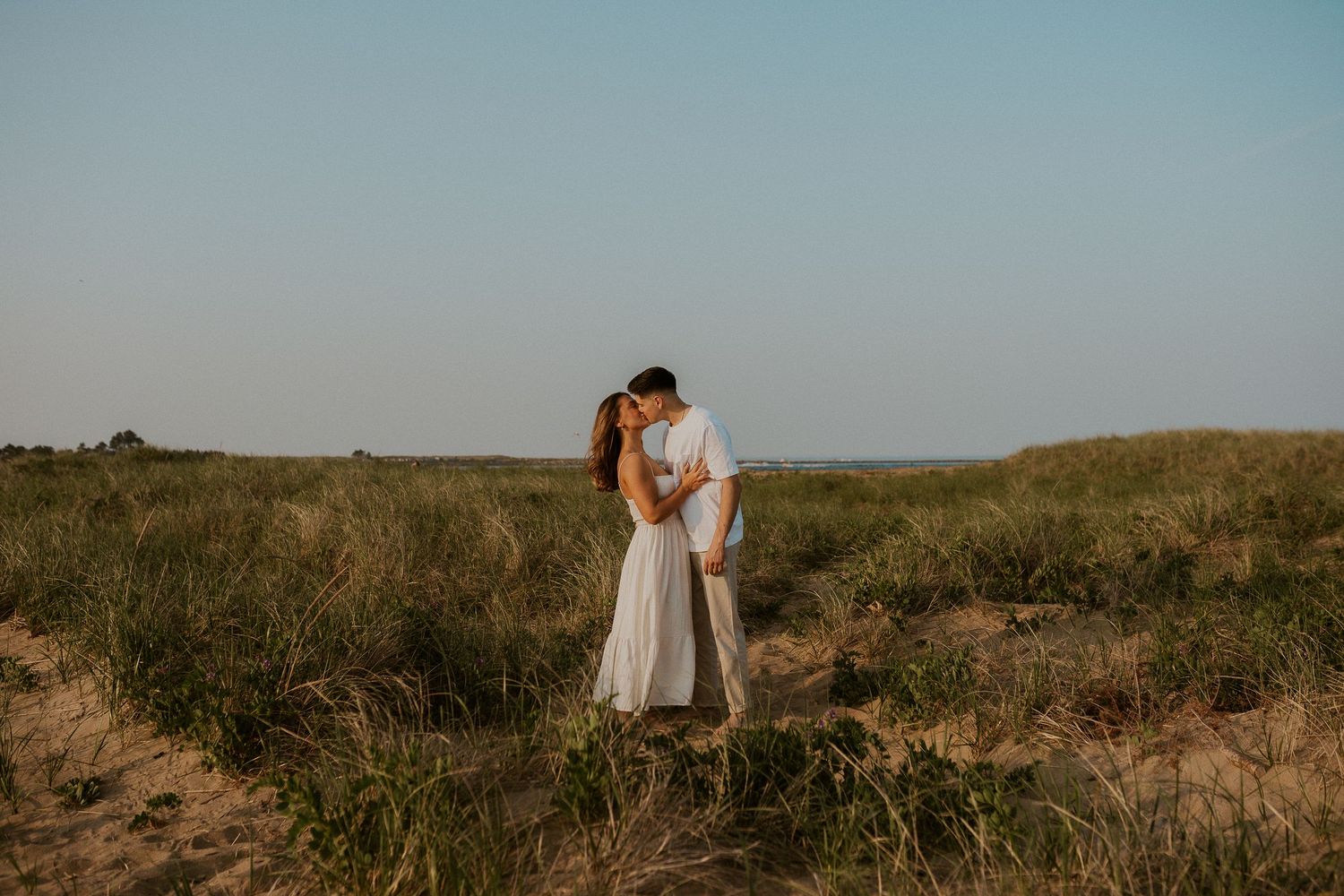 Couple embraces in a romantic moment against a golden sunset in an open prairie field.