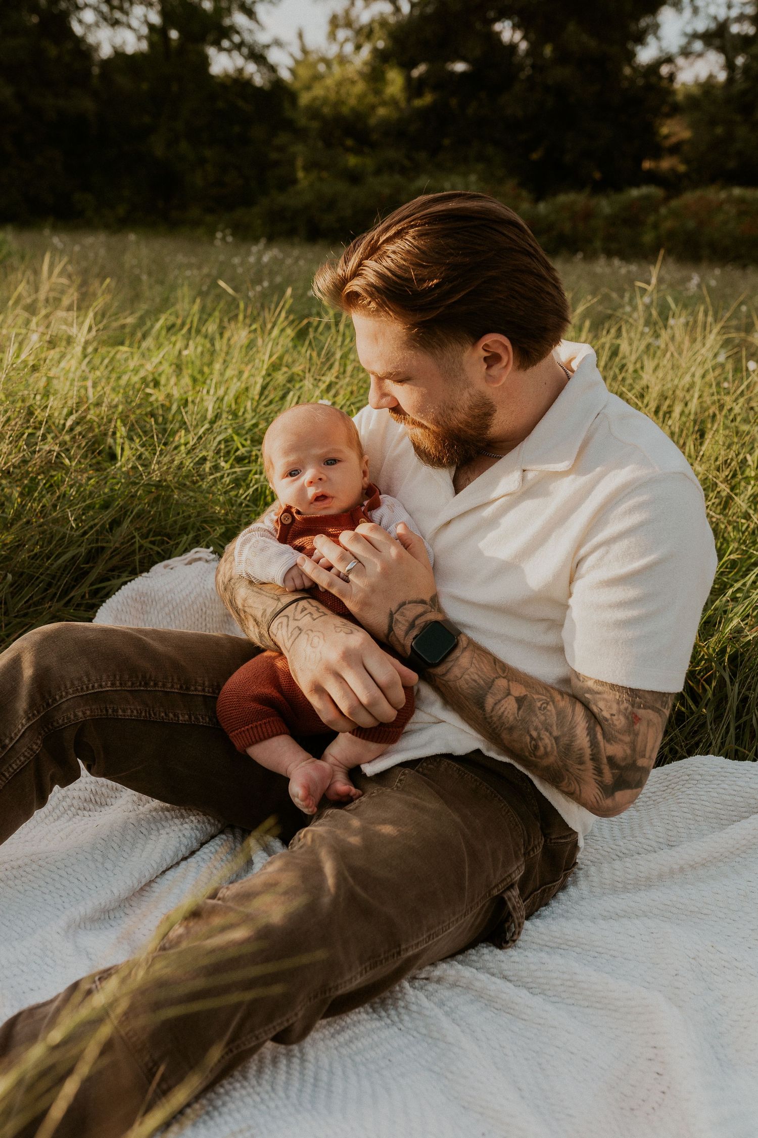 Parent and children sharing intimate moment on blanket in grassy field.
