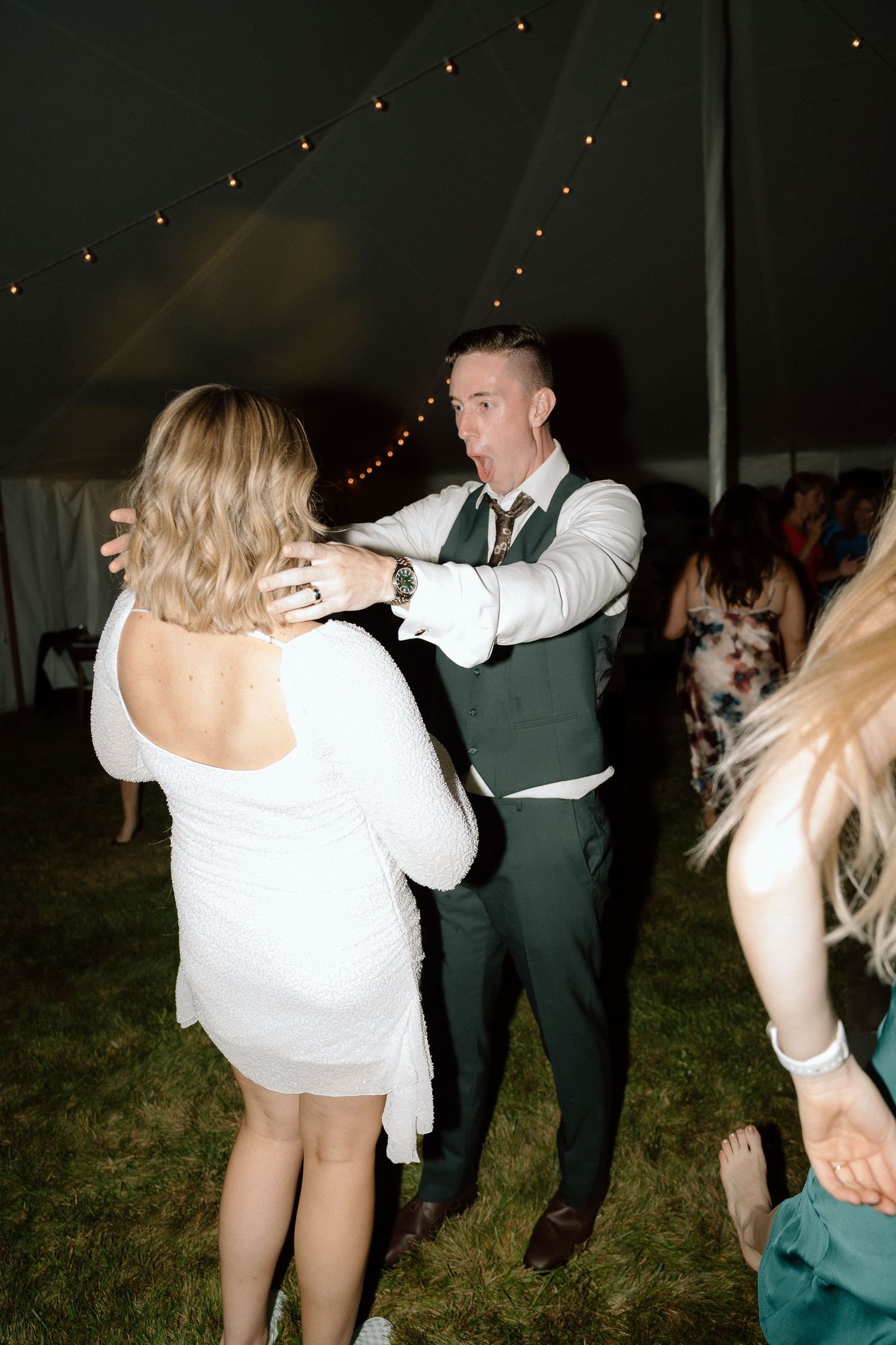 Wedding reception guests dancing energetically under a tent with string lights.