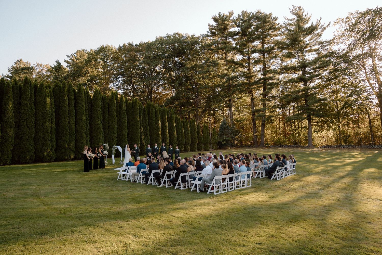 Panoramic view of outdoor wedding ceremony setup with rows of white chairs against natural landscape.