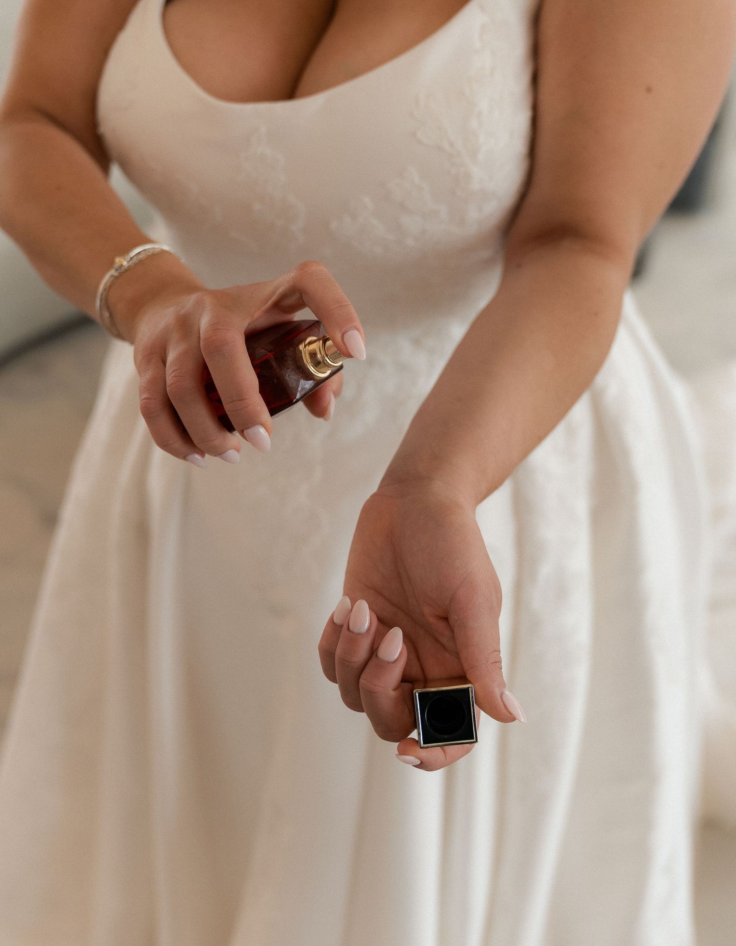 Bride in white lace gown applying perfume from a gold bottle on her wedding day.
