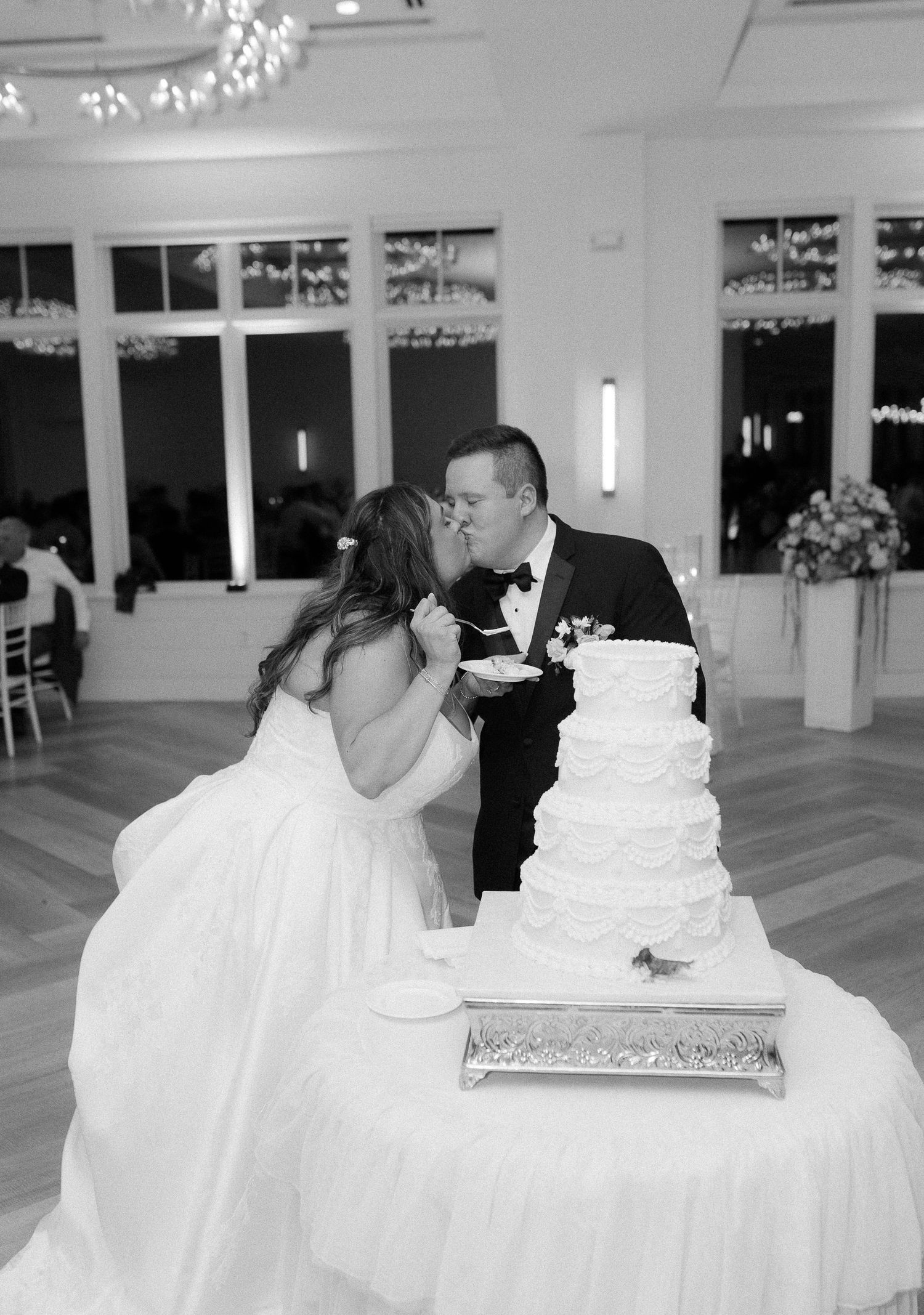 Bride and groom share a kiss while cutting tiered white wedding cake at elegant black and white reception.