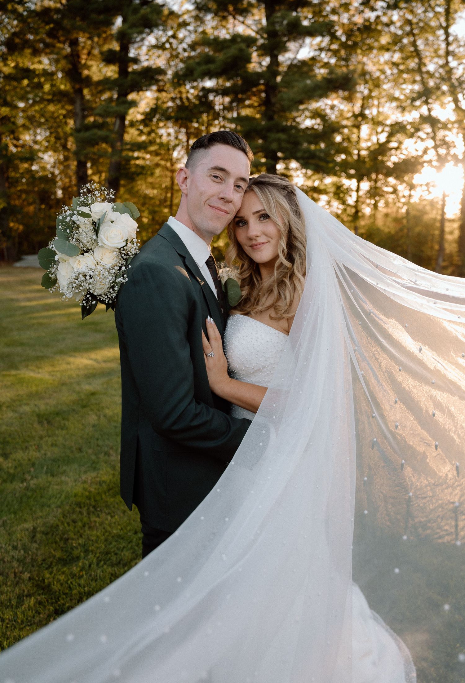 Romantic sunset portrait of newlyweds with flowing veil in golden light.