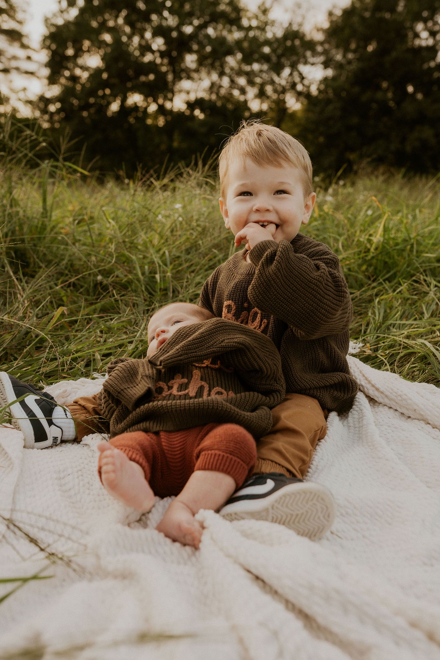 Two siblings in coordinating brown sweaters share joyful moment on blanket.
