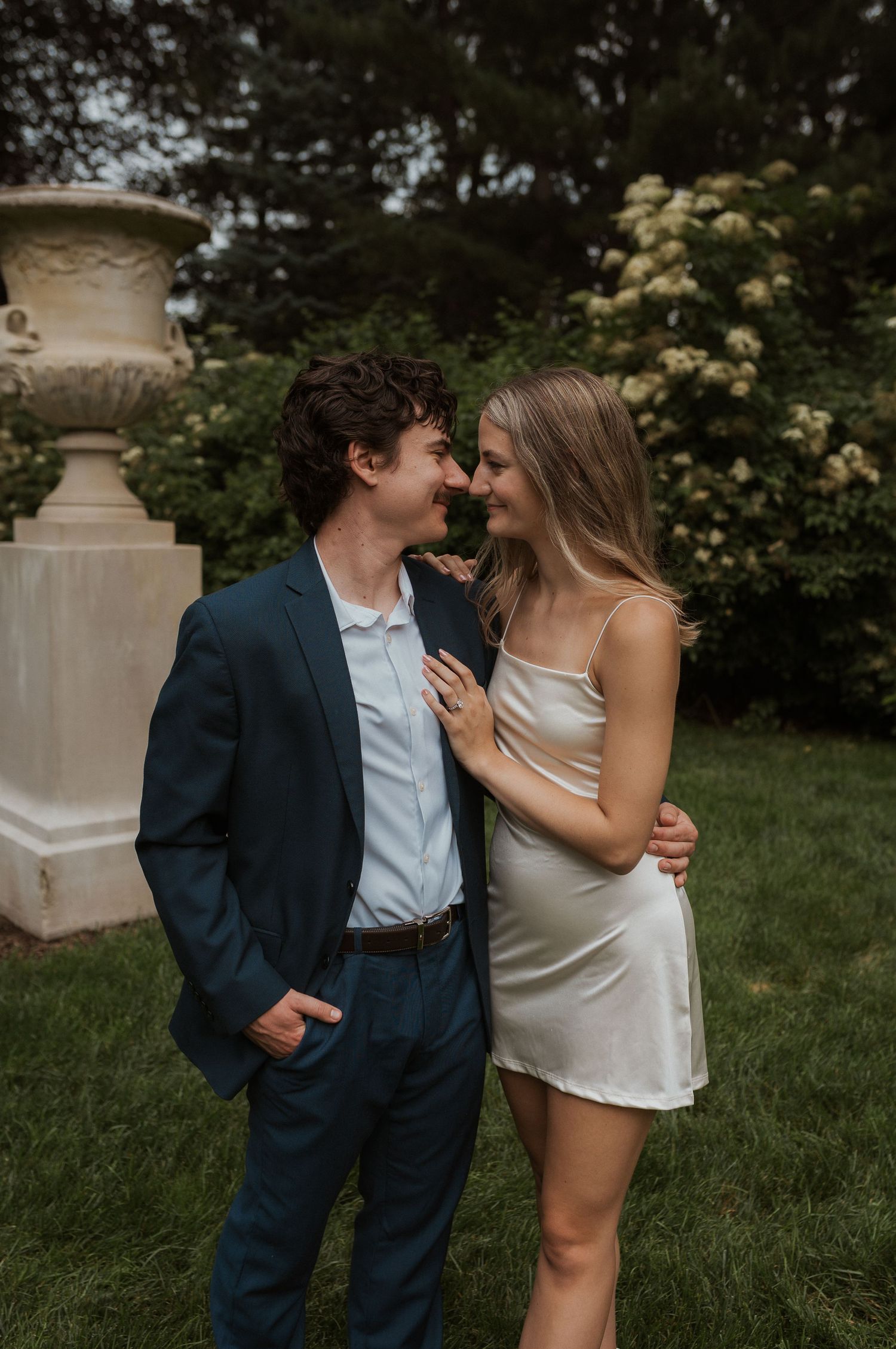 Romantic couple shares intimate moments near decorative stone pillars in a garden setting.