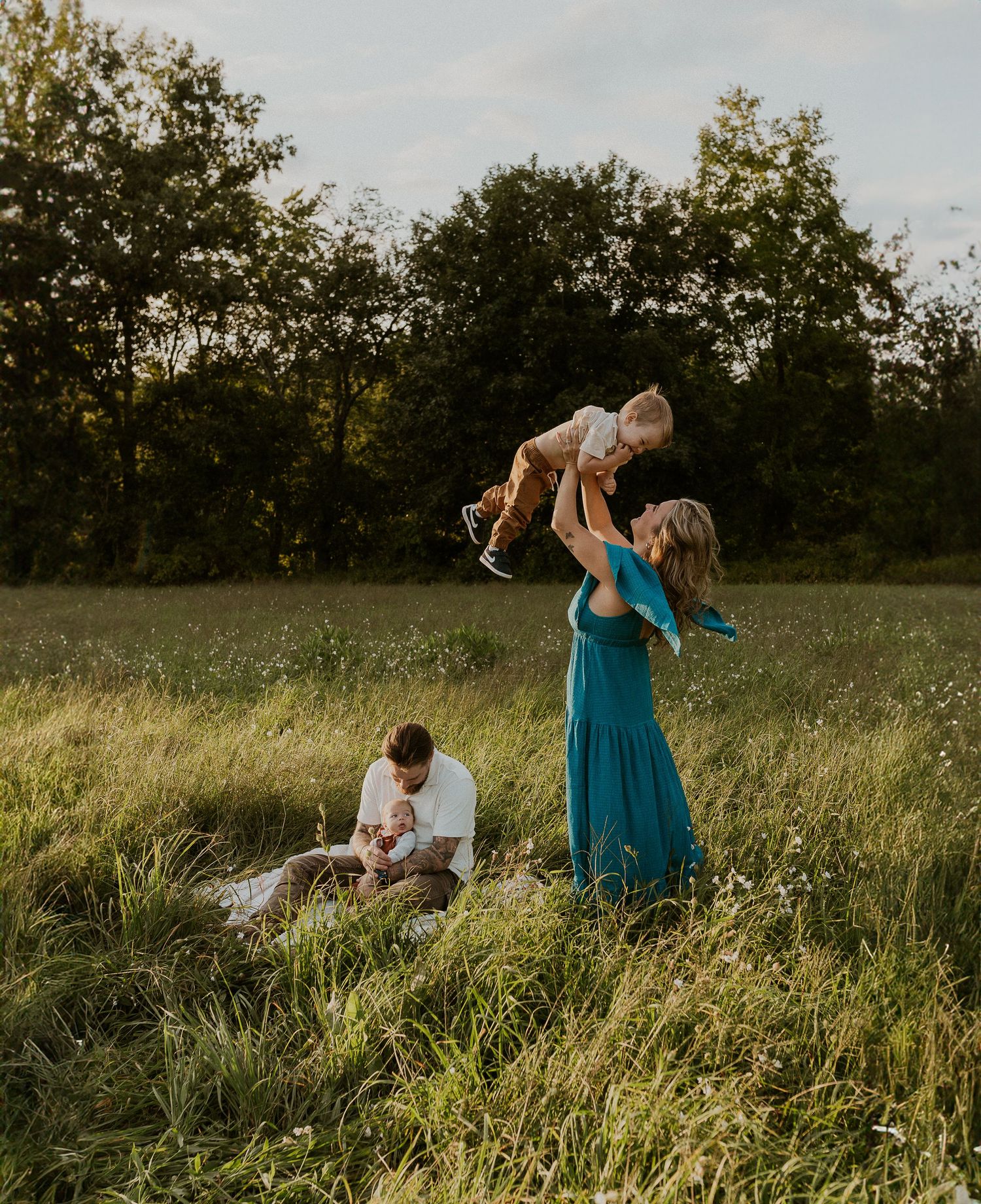 Family enjoying a sunset moment in a tall grass field with someone wearing a teal dress.