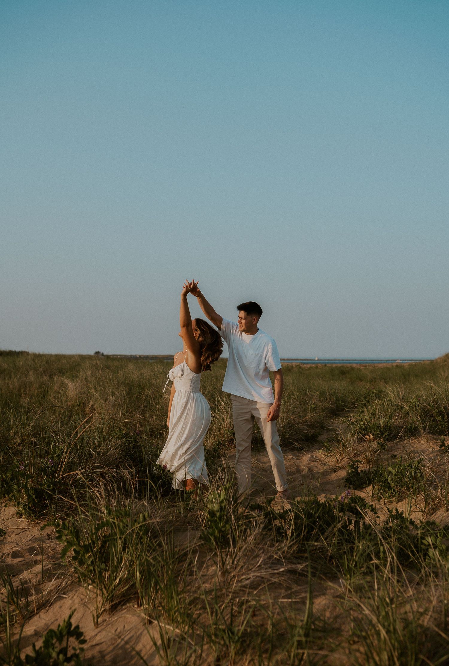 Couple dancing together on grassy dunes during golden hour.