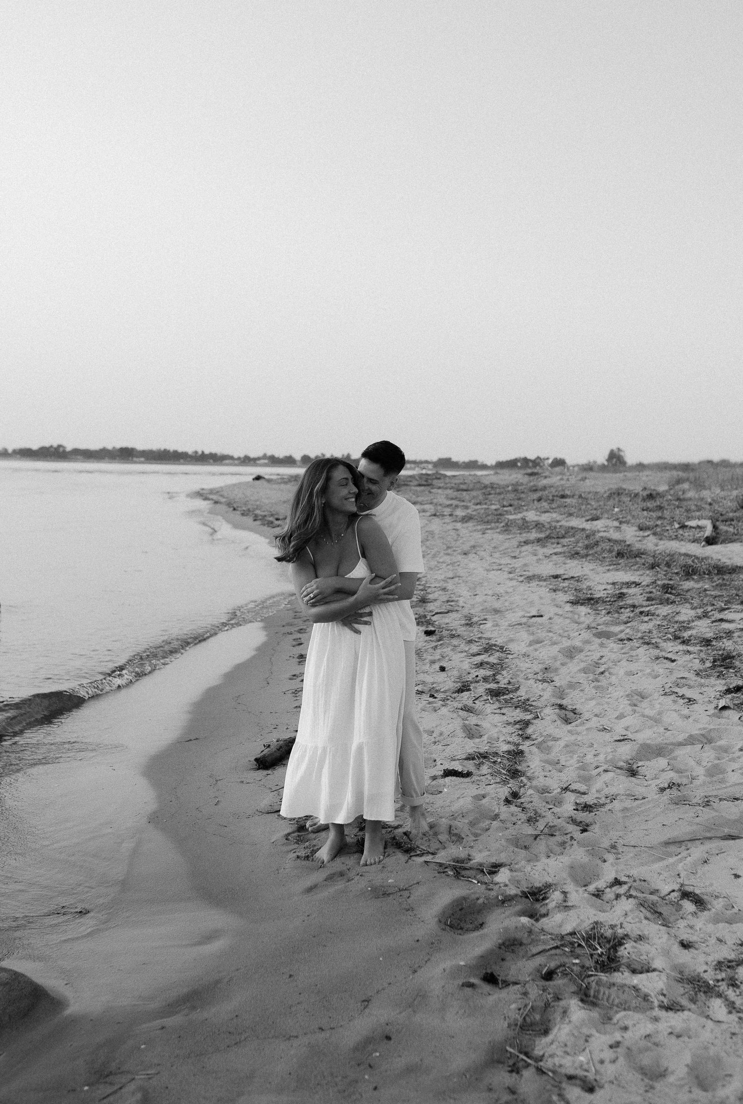 A couple embracing on a beach shoreline captured in black and white.