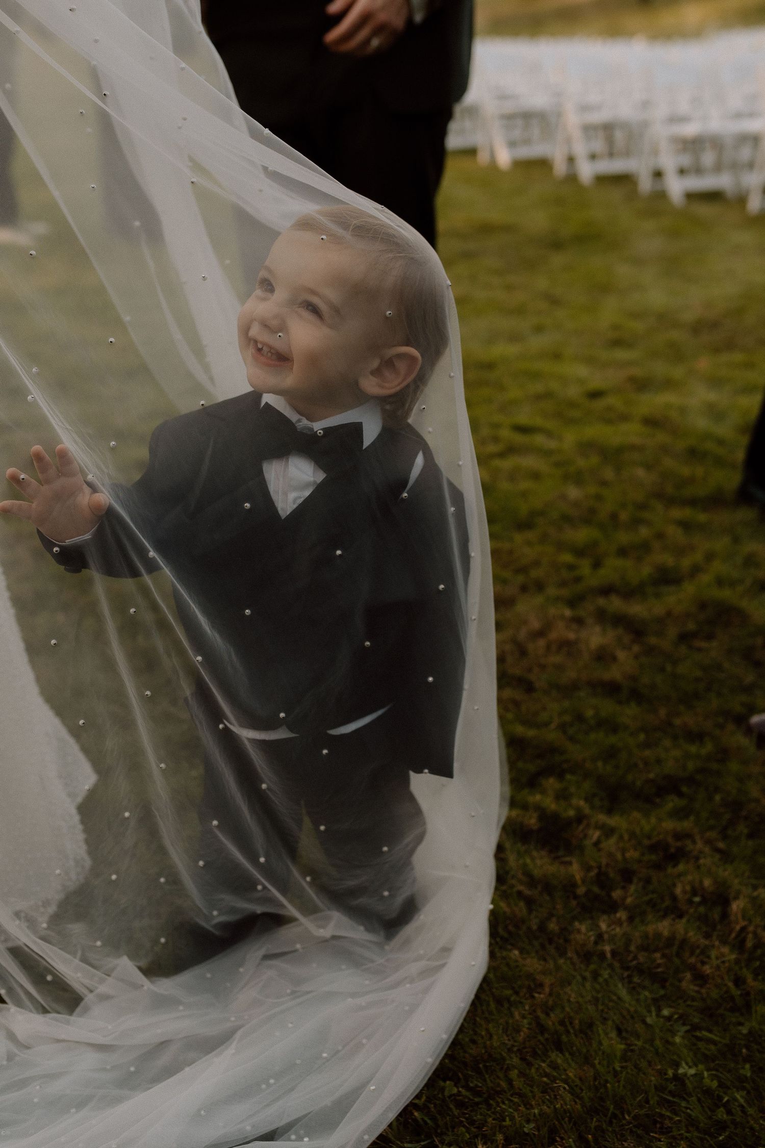 Playful moment with small child peeking through bridal veil at outdoor wedding.